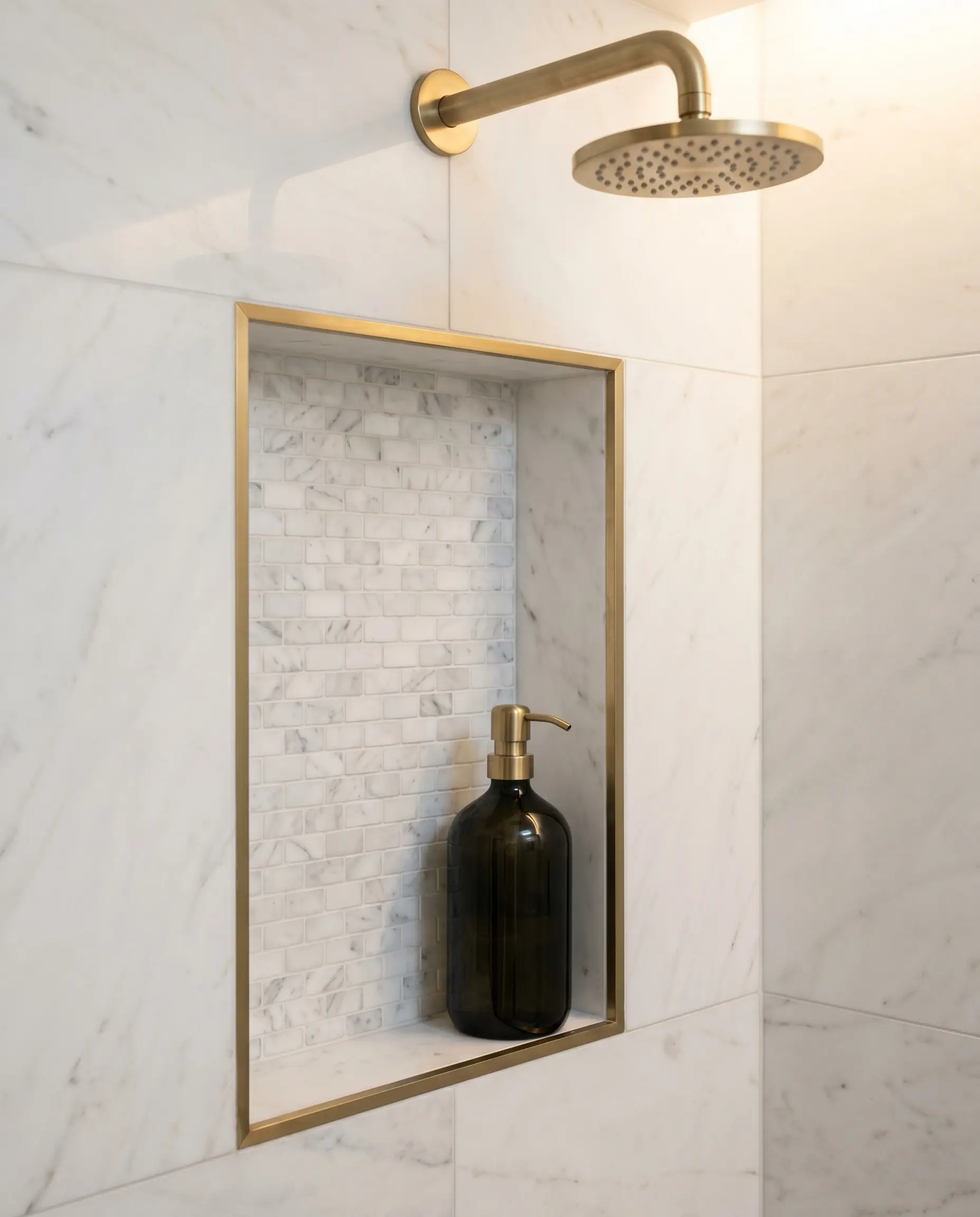 A tailored shower niche lined with white marble mosaic tiles features inside edges crisply finished with a thin brass metal trim.