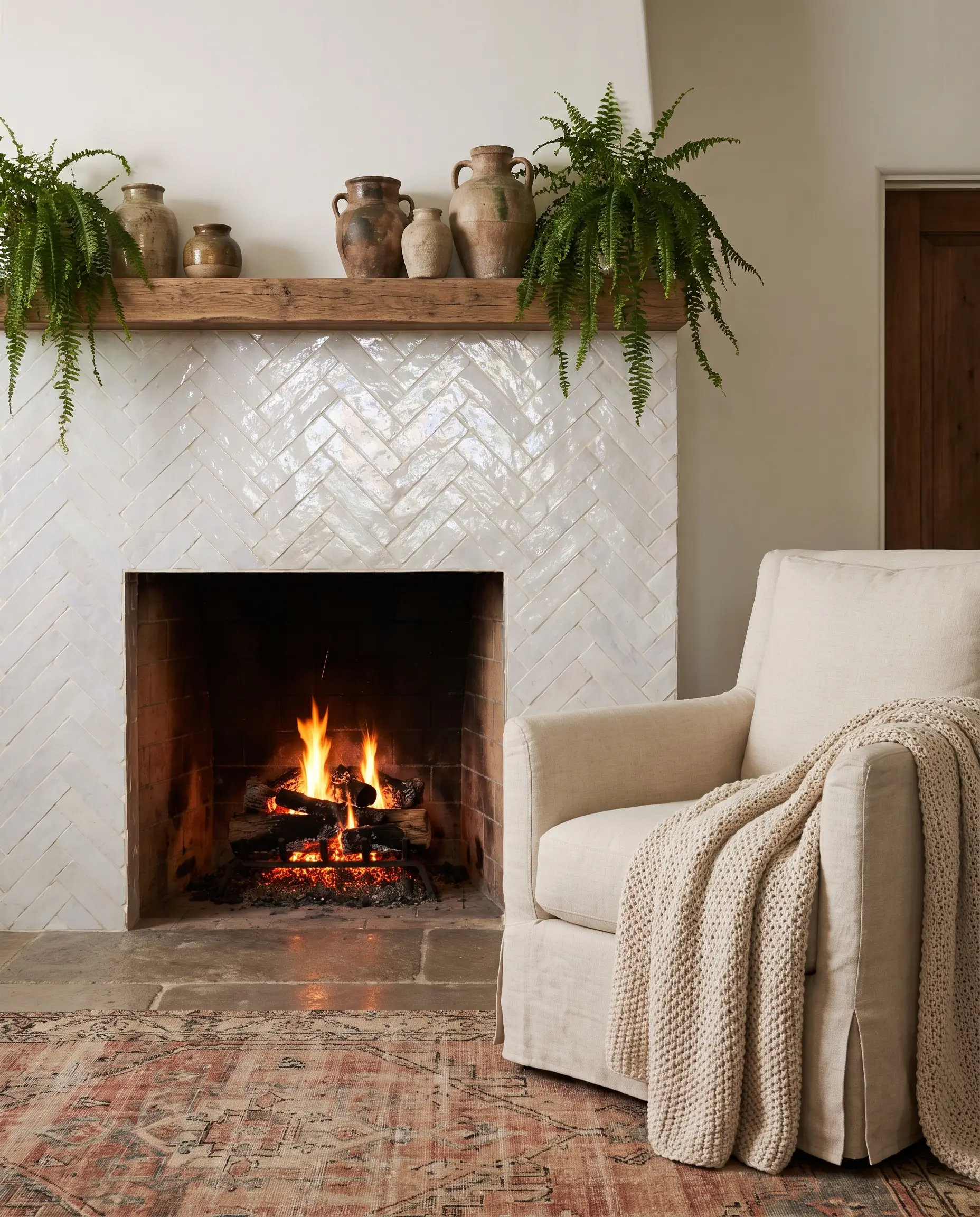 A textured fireplace surround covered in glazed white Moroccan zellige tile with cream grout sits below a raw wood mantel displaying handmade ceramic pottery.