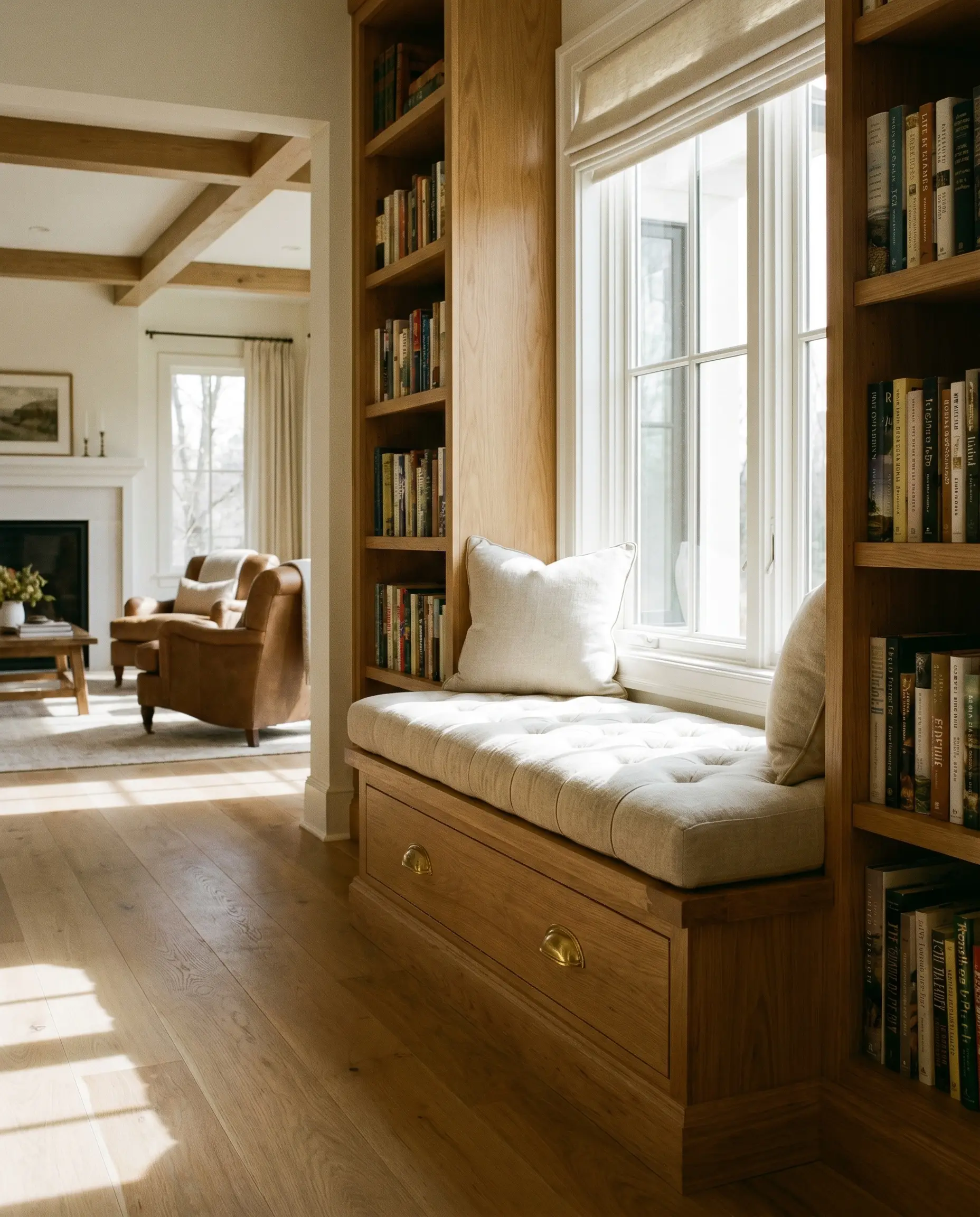An integrated window seat features a French-tufted linen bench cushion and a structural plinth drawer with solid brass cup pulls, flanked by bookshelves.