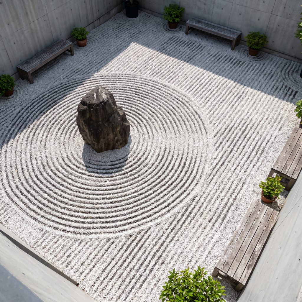 Tight concentric circular samon ripples in white crushed gravel surround the base of a large natural cleft anchor stone in a minimalist courtyard.