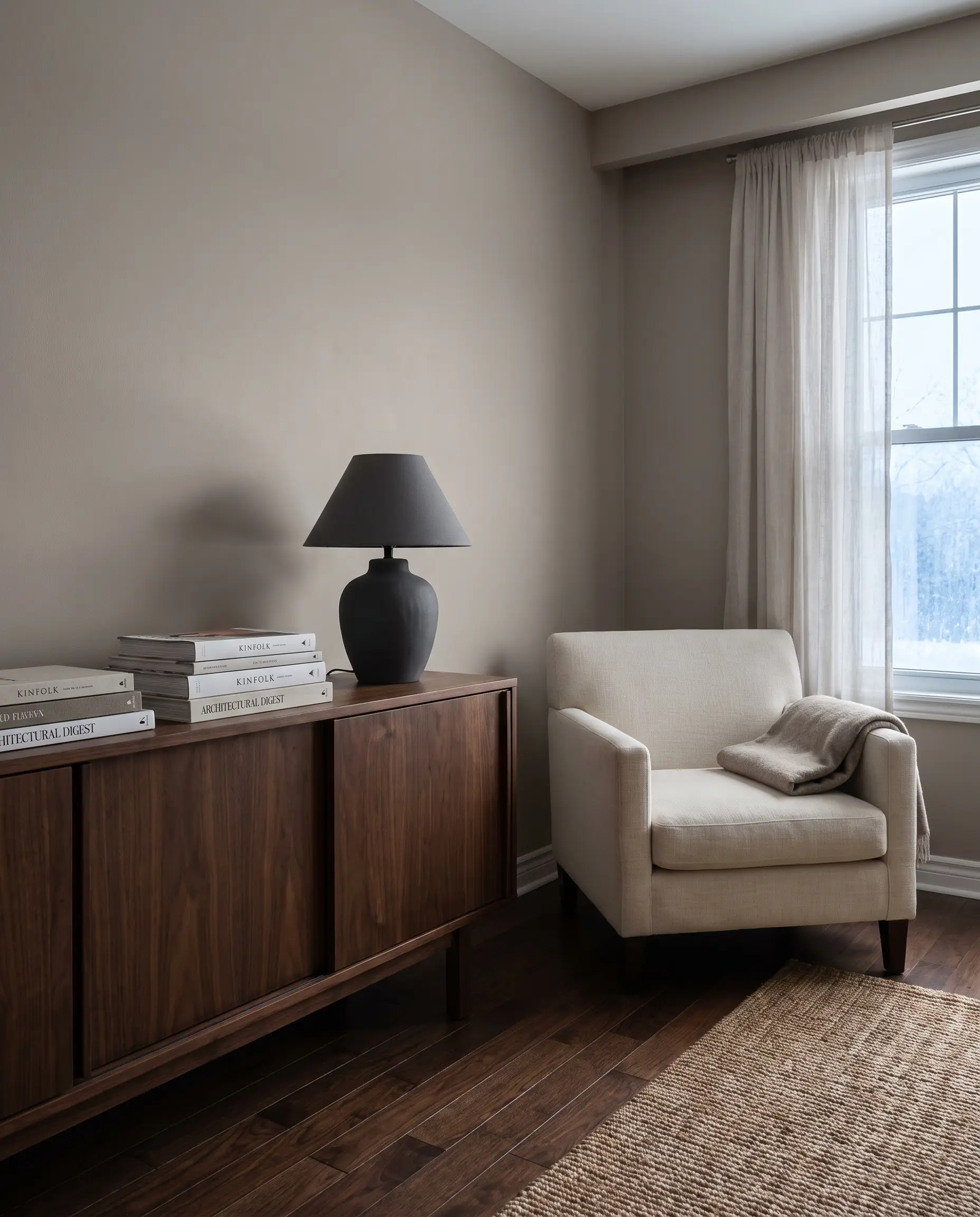 A mid-century walnut credenza and matte ceramic table lamp sit against walls showcasing the best Behr gray paint colors.