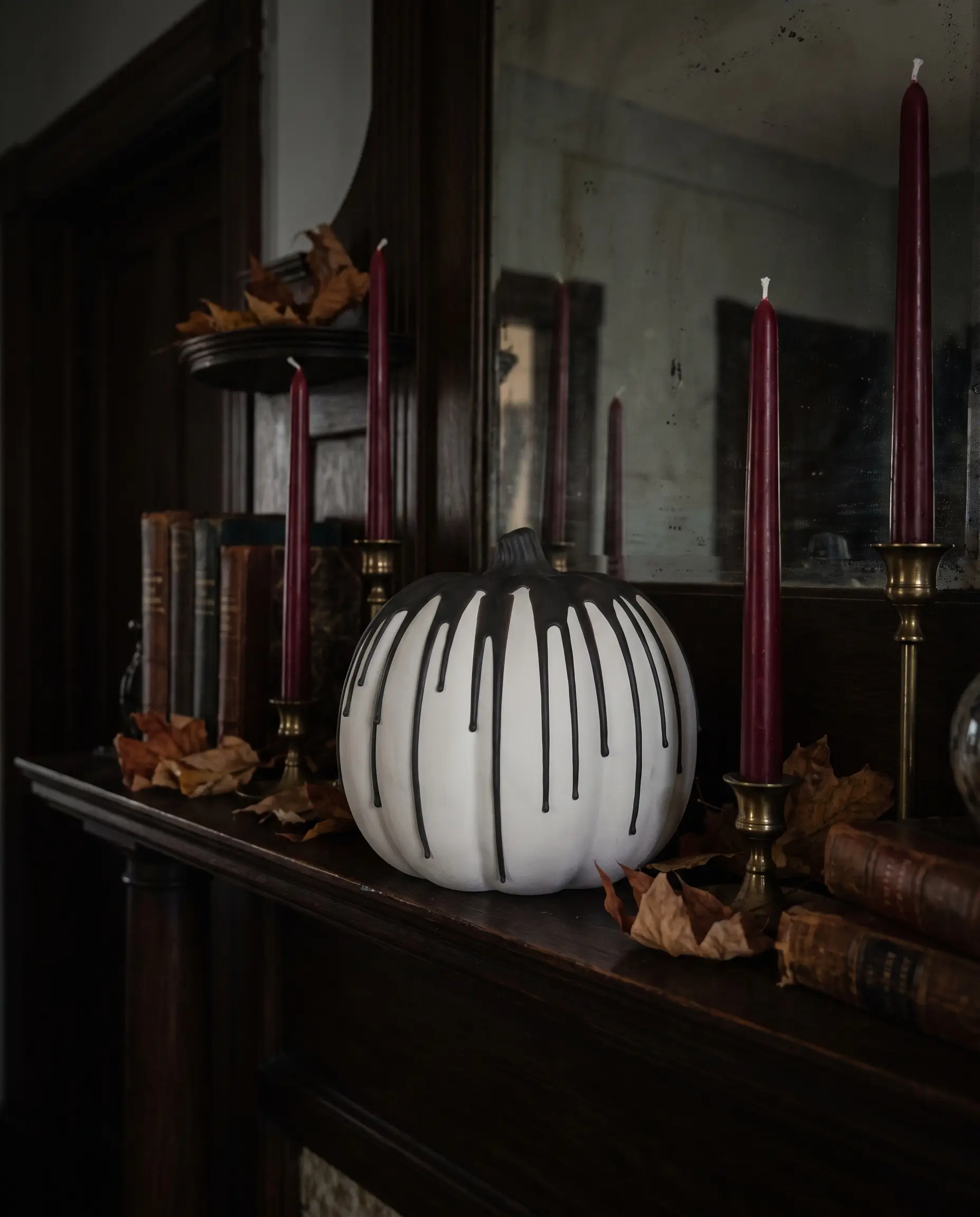Heavy Benjamin Moore Black Beauty wax drips down the sides of a matte white faux pumpkin placed beside deep crimson taper candles on a mantelpiece.