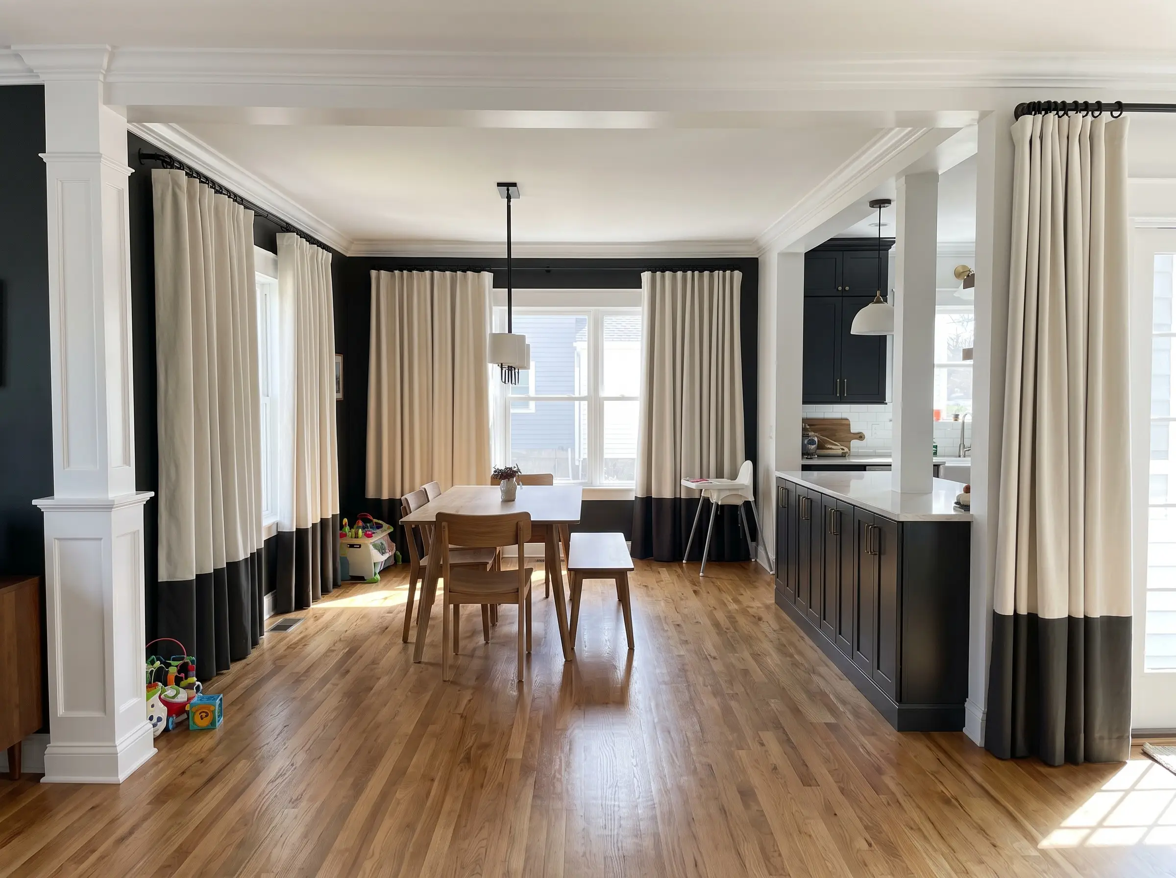 Heavy cotton canvas panels color-blocked in Alabaster and Greenblack hang from matte black rings on a sleek French return rod over warm wood flooring.