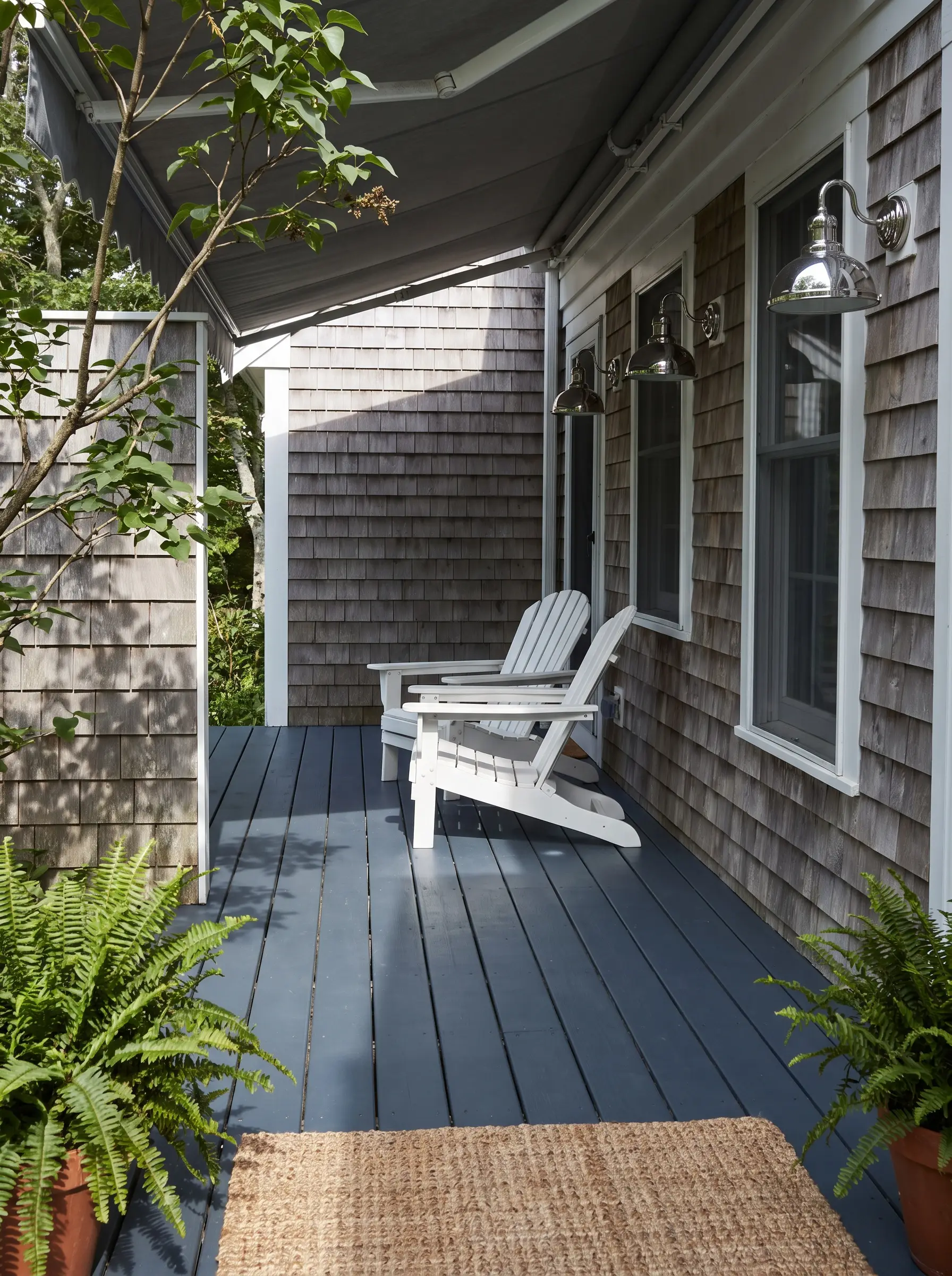 Classic crisp white Adirondack chairs sit on a dark English Channel painted porch floor illuminated by polished chrome exterior wall sconces.
