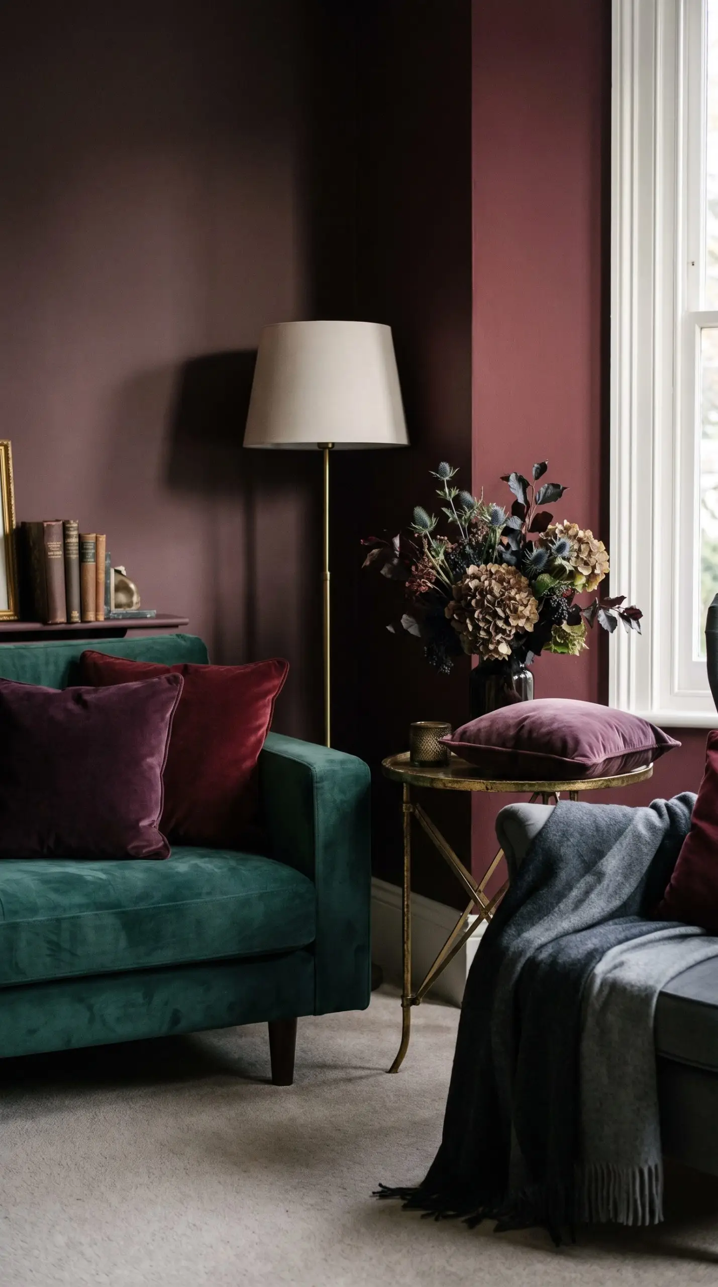 Deep plum, oxblood, and smoked emerald textiles sit on a modest side table against carnelian and dark burgundy painted walls for 2026 halloween decor.