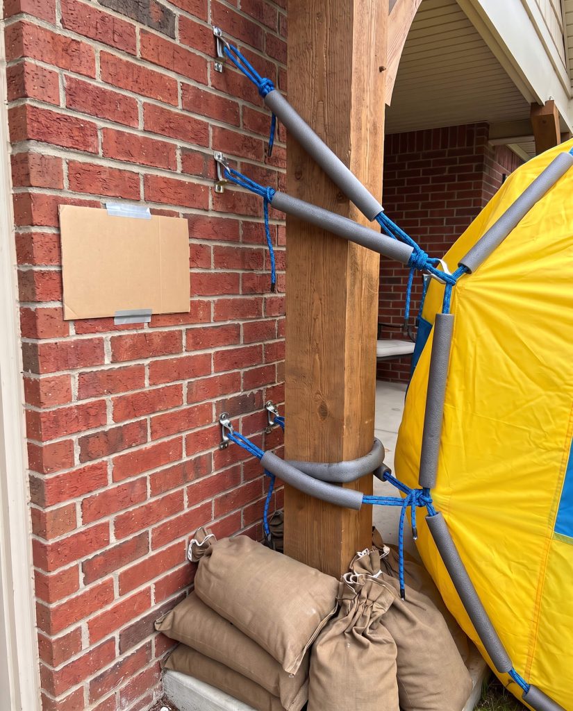 Heavy-duty brick clips, paracord tension lines, and canvas sandbags secure a massive inflatable to exterior masonry for 2026 outdoor Halloween decorating.