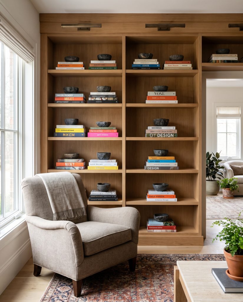 Custom bookcase millwork showcases horizontal stacking of large coffee table books, each topped with a single contrasting sculptural stone bowl.