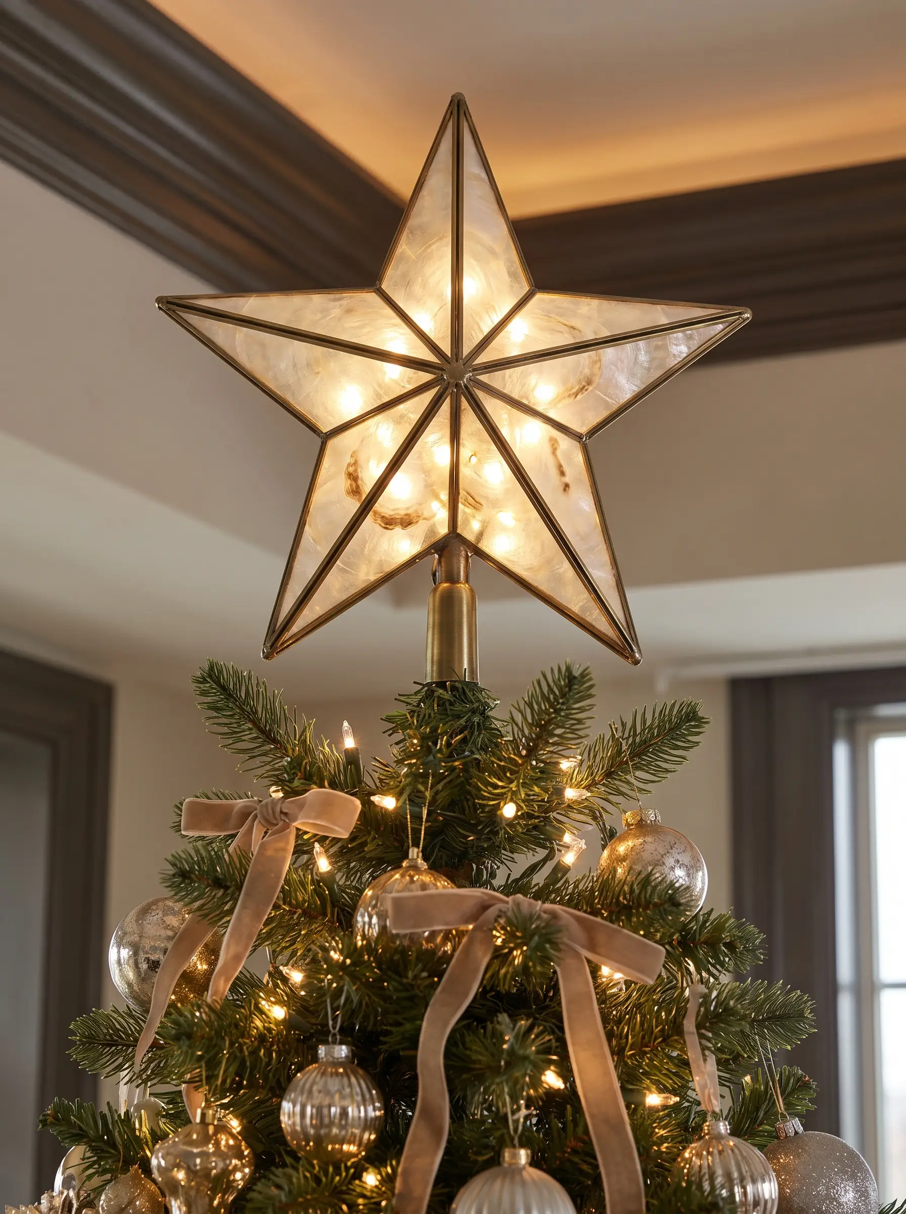 An oversized brass-framed Capiz shell star topper stands perfectly rigid at the peak of a majestic fir, backlit by a cluster of warm white lights.