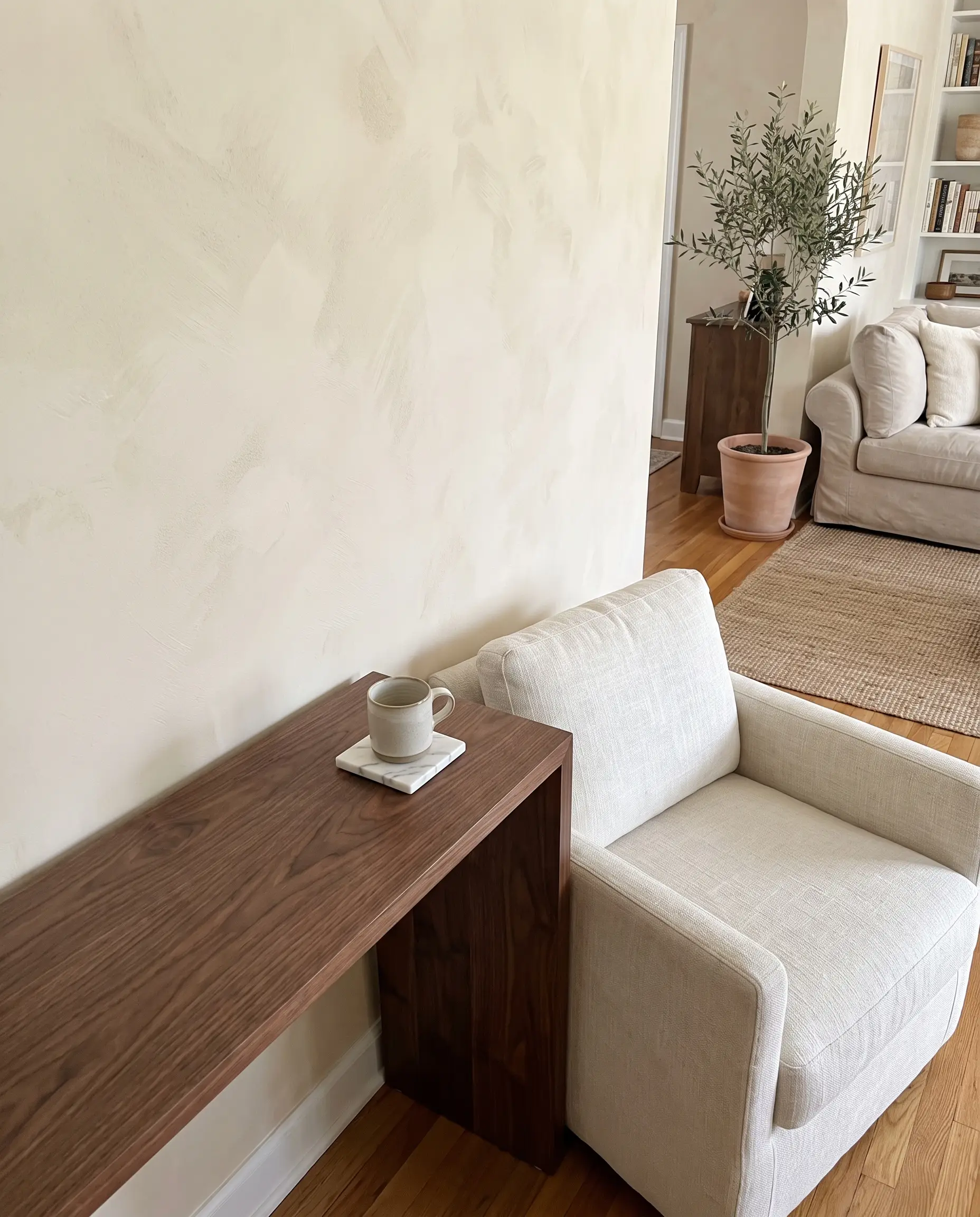 A solid walnut console table holding a honed Calacatta marble coaster stands against a Bauwerk Colour Bone limewash wall beside a heavy linen lounge chair.