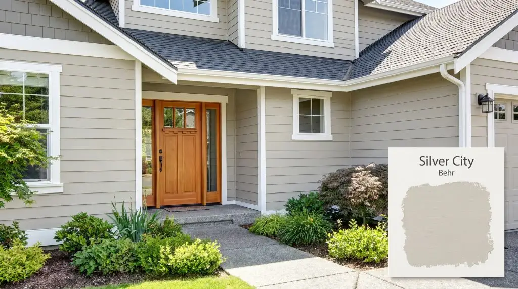 Crisp white trim and a natural wood front door highlight modern exterior siding painted in Behr Silver City (Hex #c8c8c2) surrounded by lush landscaping.