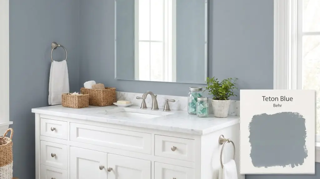 A serene bathroom vanity featuring white marble countertops and brushed nickel hardware is backed by a dusty blue Behr Teton Blue (Hex #8d99a1) wall.