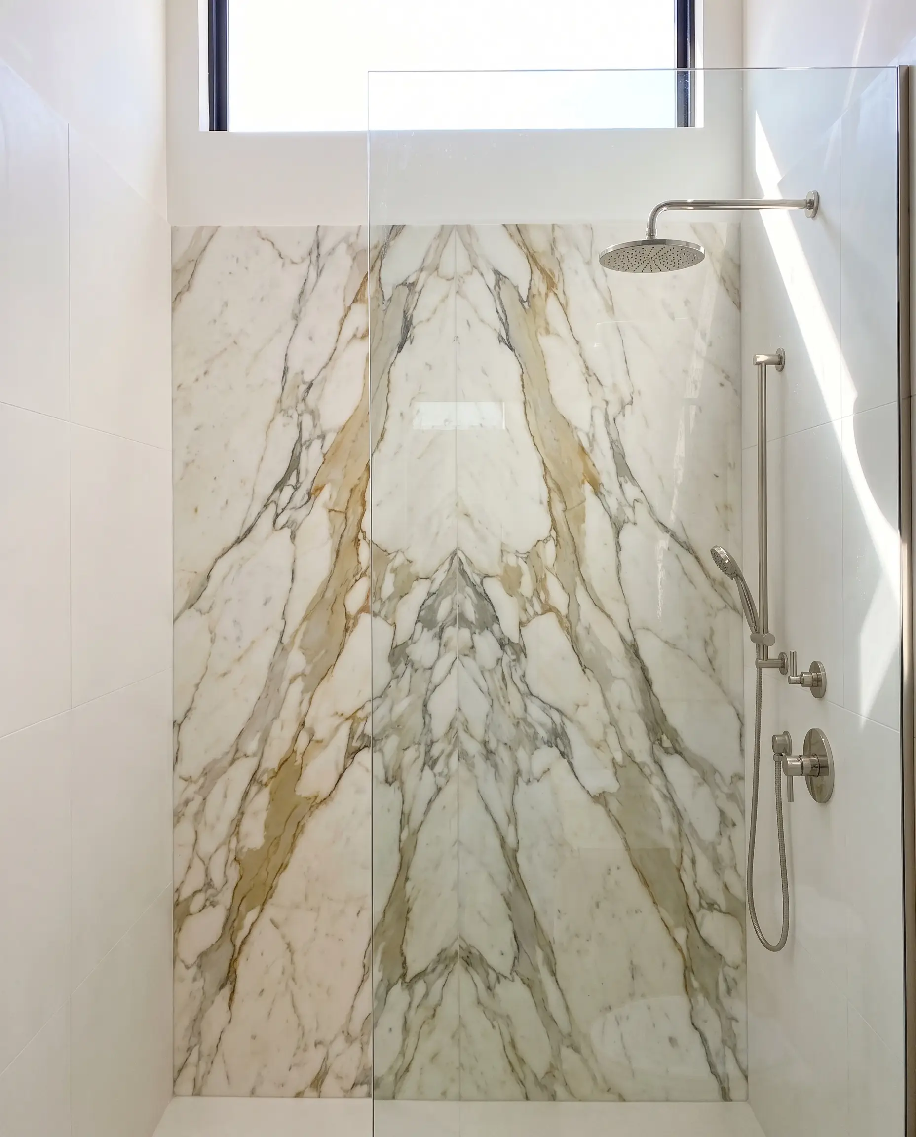 A continuous bookmatched Calacatta Borghini marble slab wall with heavy gold veining anchors this modern marble bathroom design shower enclosure featuring polished nickel fixtures.