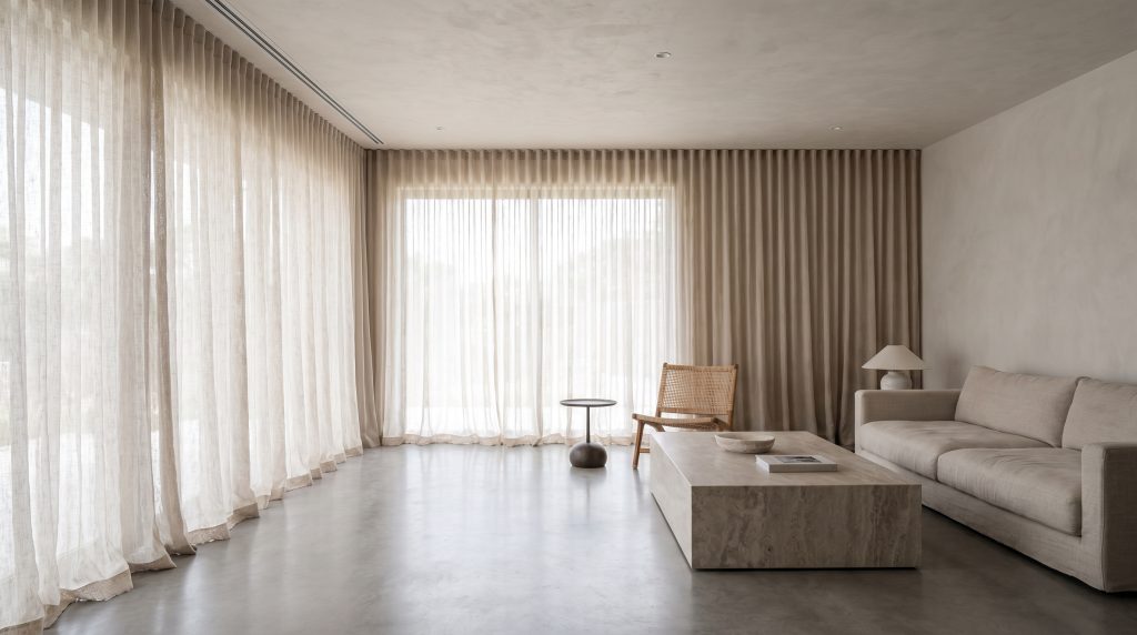 Continuous ceiling-to-floor sheer linen drapery hangs from a recessed track behind a monolithic stone coffee table and low-profile sofa in a modern minimalist living room.