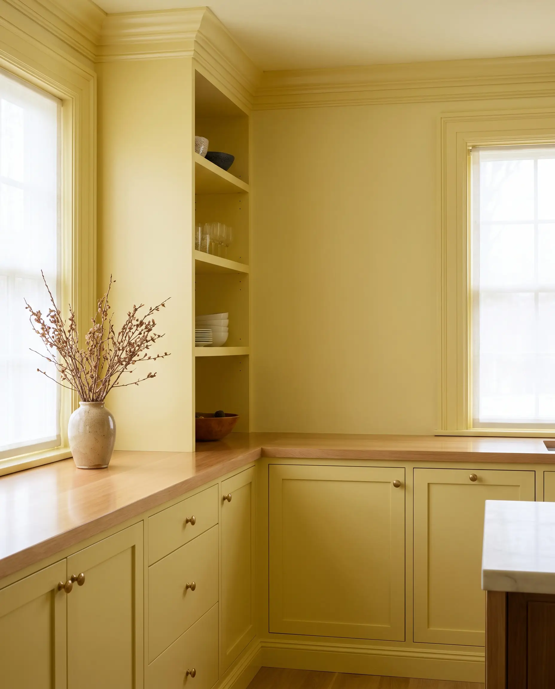 Flat pale lemon walls meet semi-gloss crown molding and baseboards in a seamless color drenching application within this transitional yellow kitchen corner.