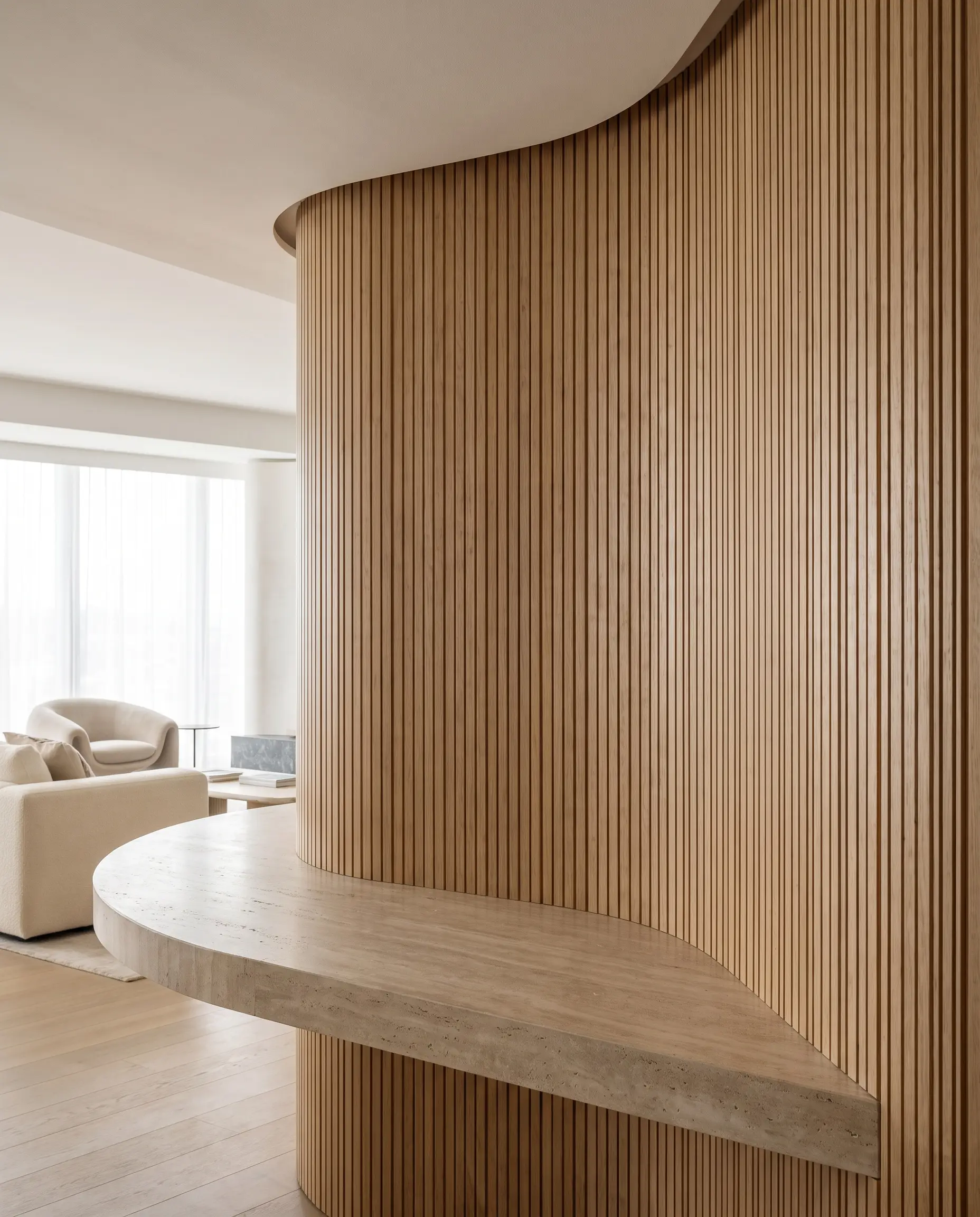 A sweeping curved architectural wall clad in flexible wooden wall panels anchors a thick honed travertine countertop acting as a sculptural entryway console.