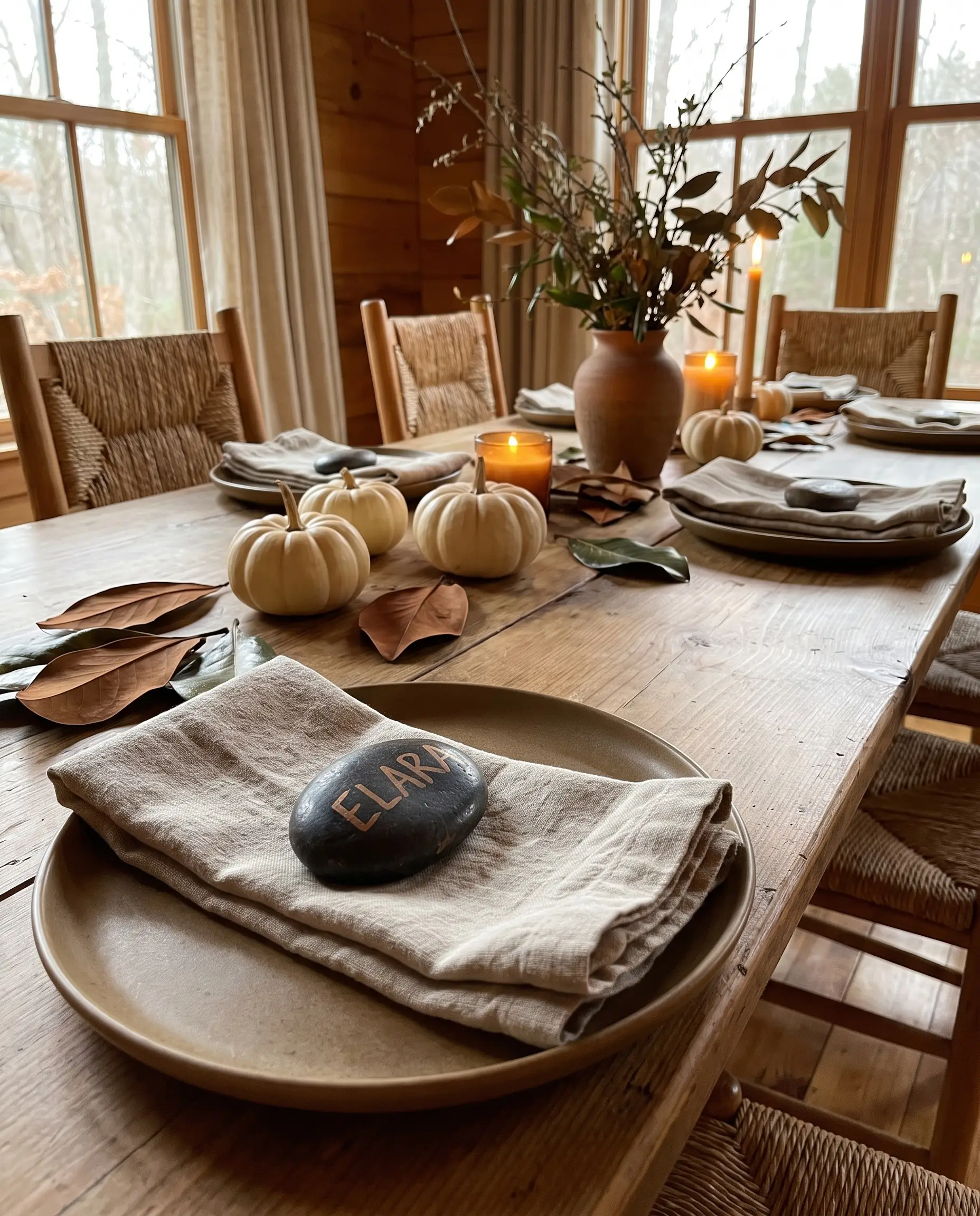 A smooth dark river stone resting on a folded linen napkin and matte ceramic plate serves as a personalized place card alongside foraged magnolia leaves.