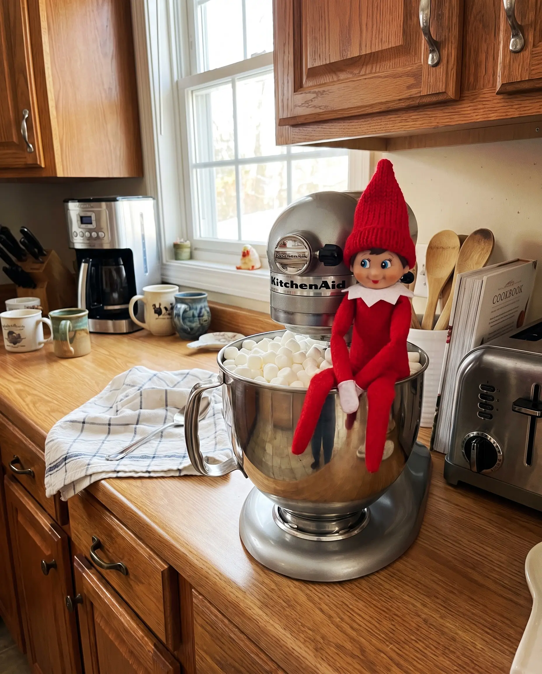 Un elfo natalizio immerso nei mini marshmallow nella ciotola in acciaio inox dell'impastatrice KitchenAid.