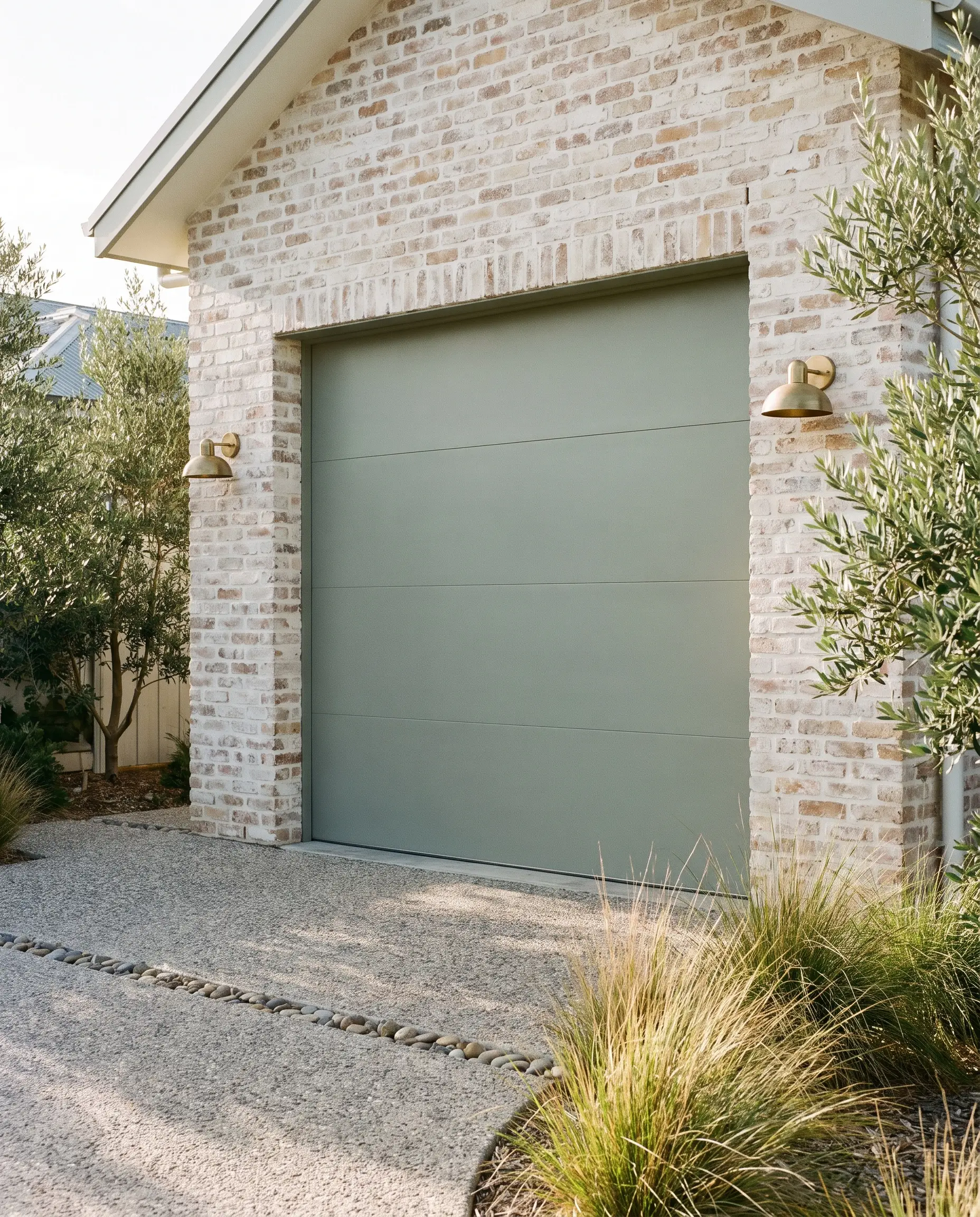 Embodying garage door trends 2027, a modern door painted in Farrow & Ball Pigeon pairs with unlacquered brushed brass sconces and a limewash brick wall.