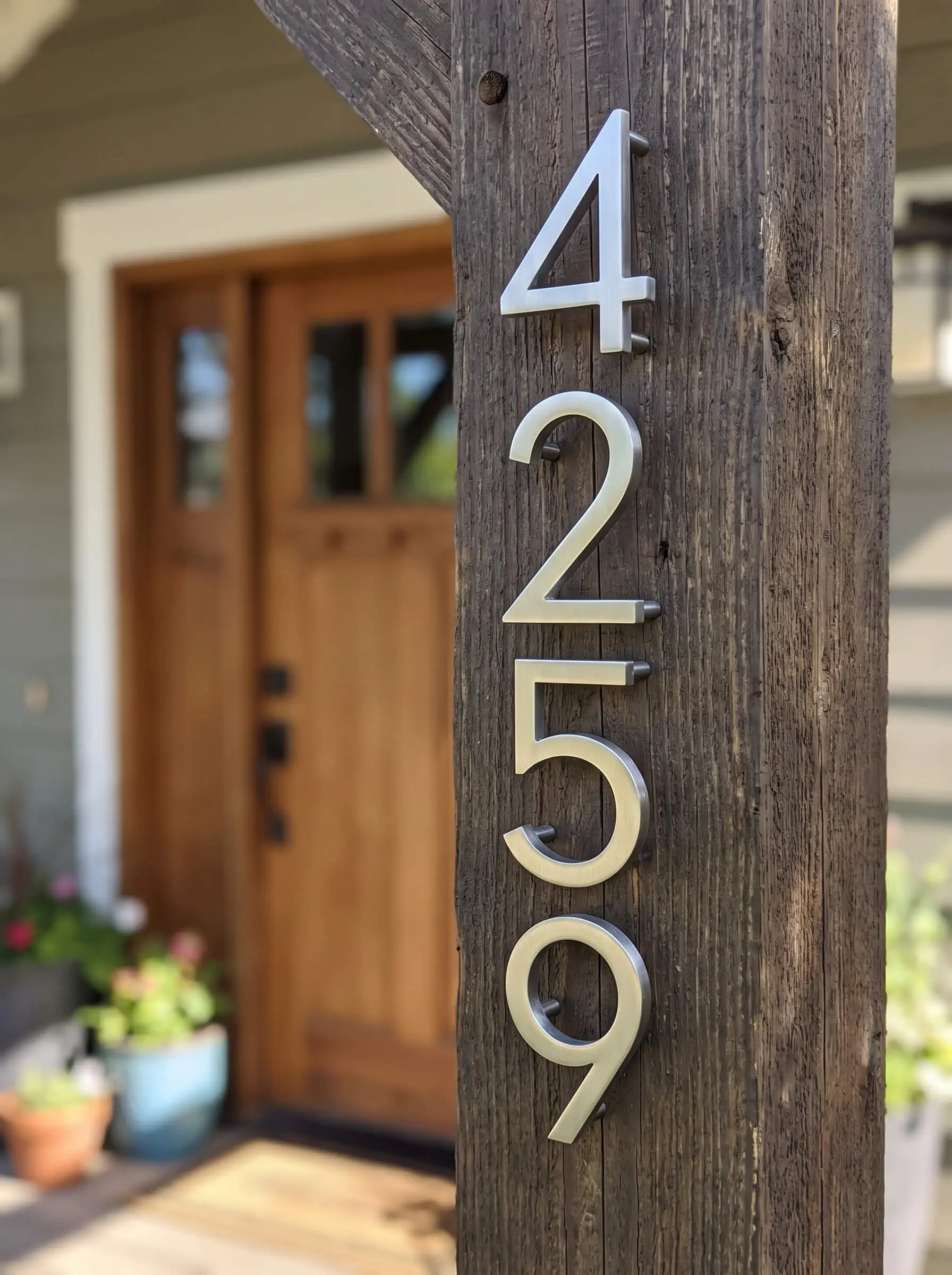 Crisp, 6-inch floating san-serif metal house numbers machined from solid stainless steel are mounted vertically on a structural wooden porch column.