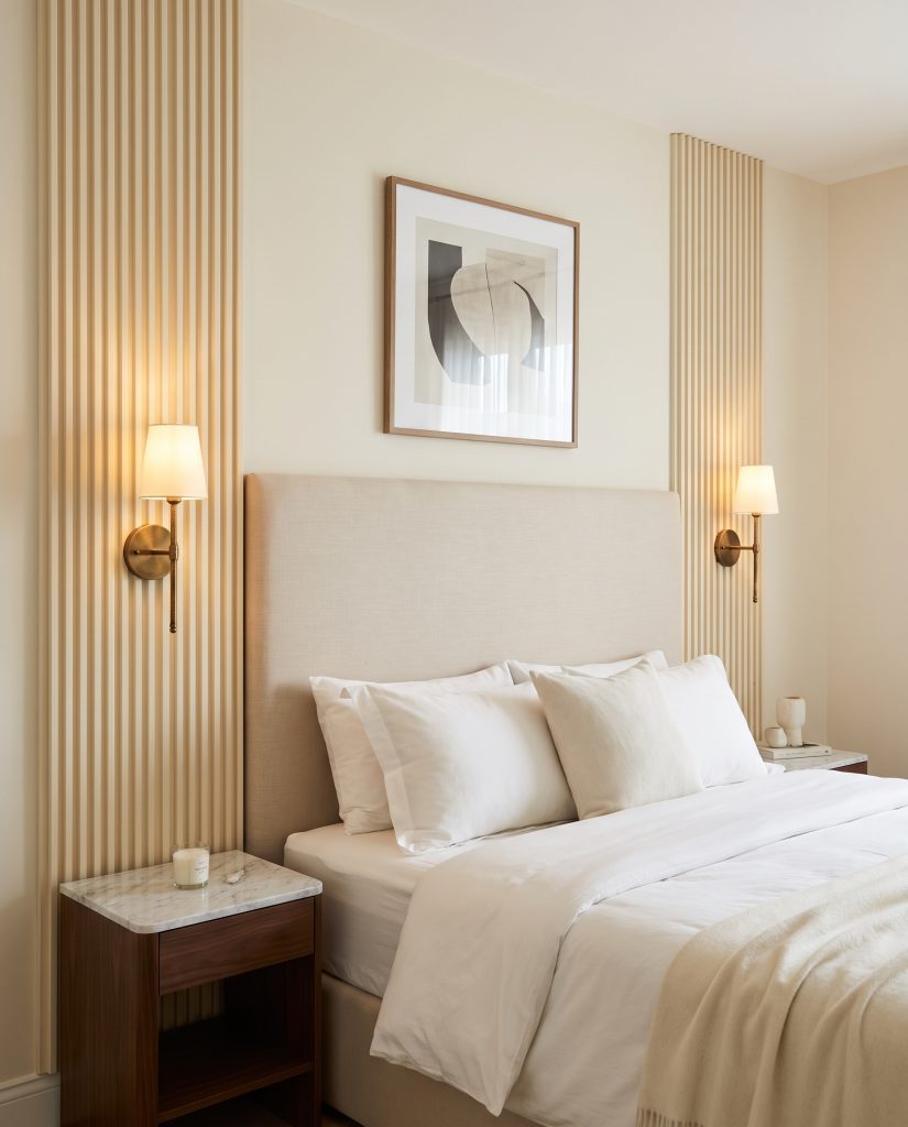 Narrow vertical strips of fluted MDF texture act as architectural columns framing an upholstered headboard, mounting aged brass sconces above marble-topped nightstands.