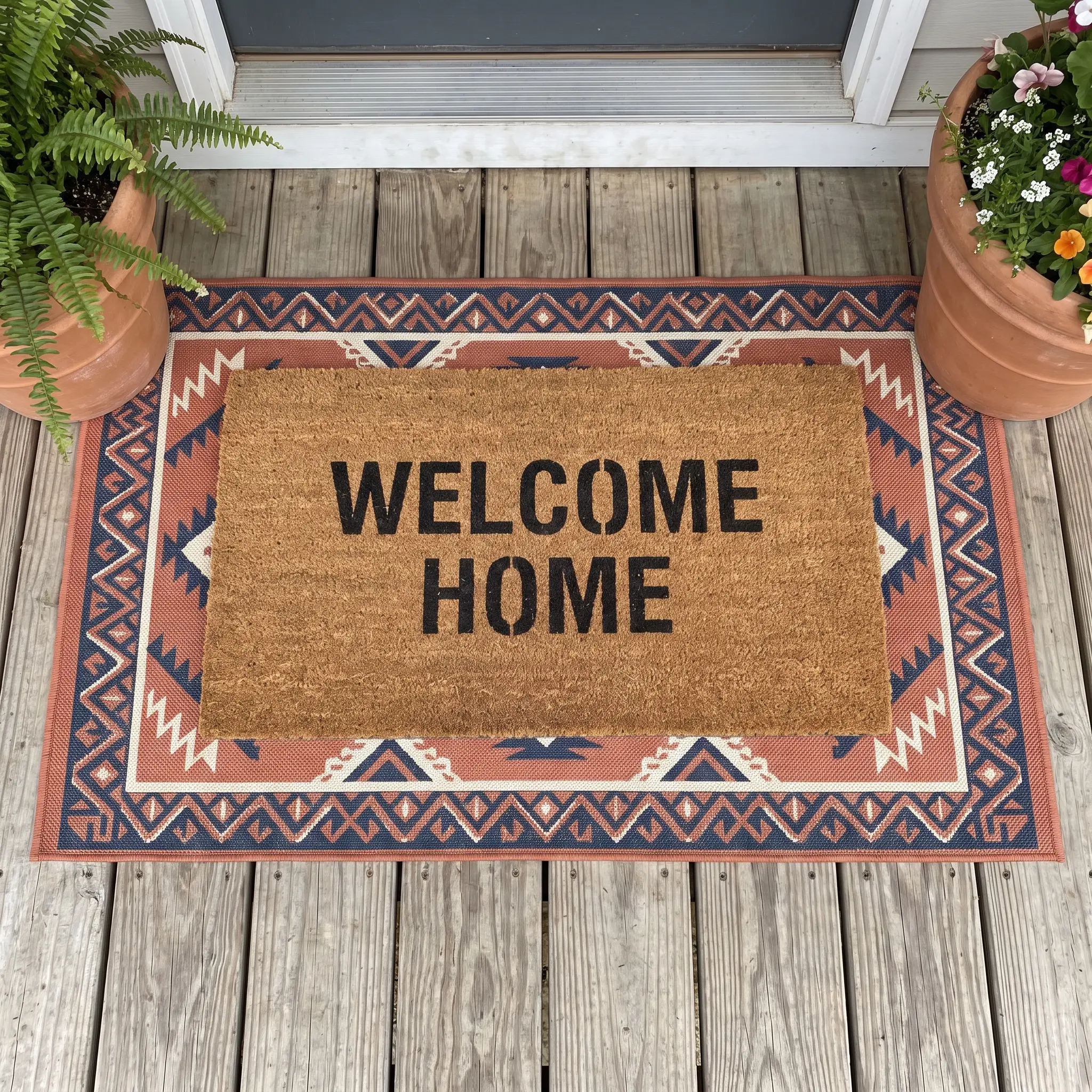 Coir mat layering over a patterned flat-weave synthetic base rug at the threshold of a front door, creating a textured, high-traffic entryway.