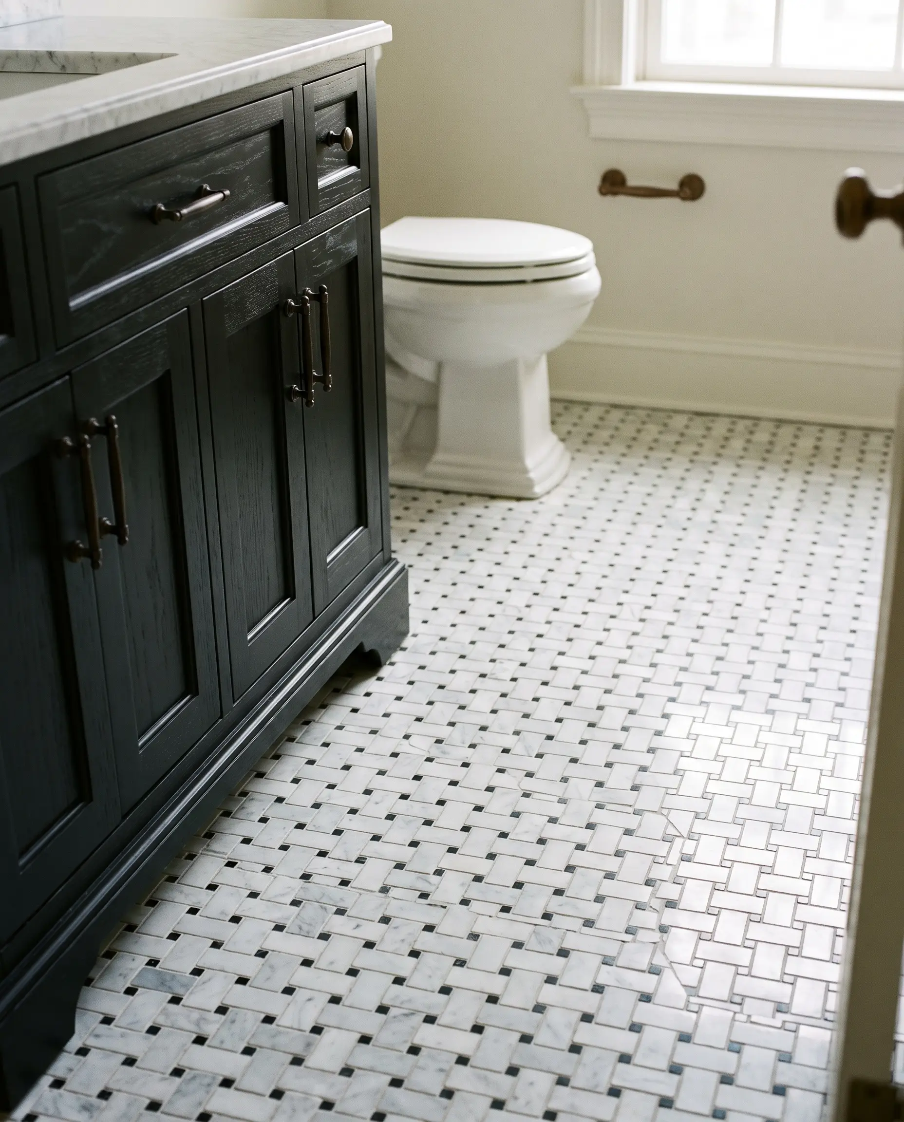 A dense Carrara and Nero Marquina marble basketweave mosaic floor with black dot inserts sits beneath an ebony woodwork vanity base and dark bronze hardware.
