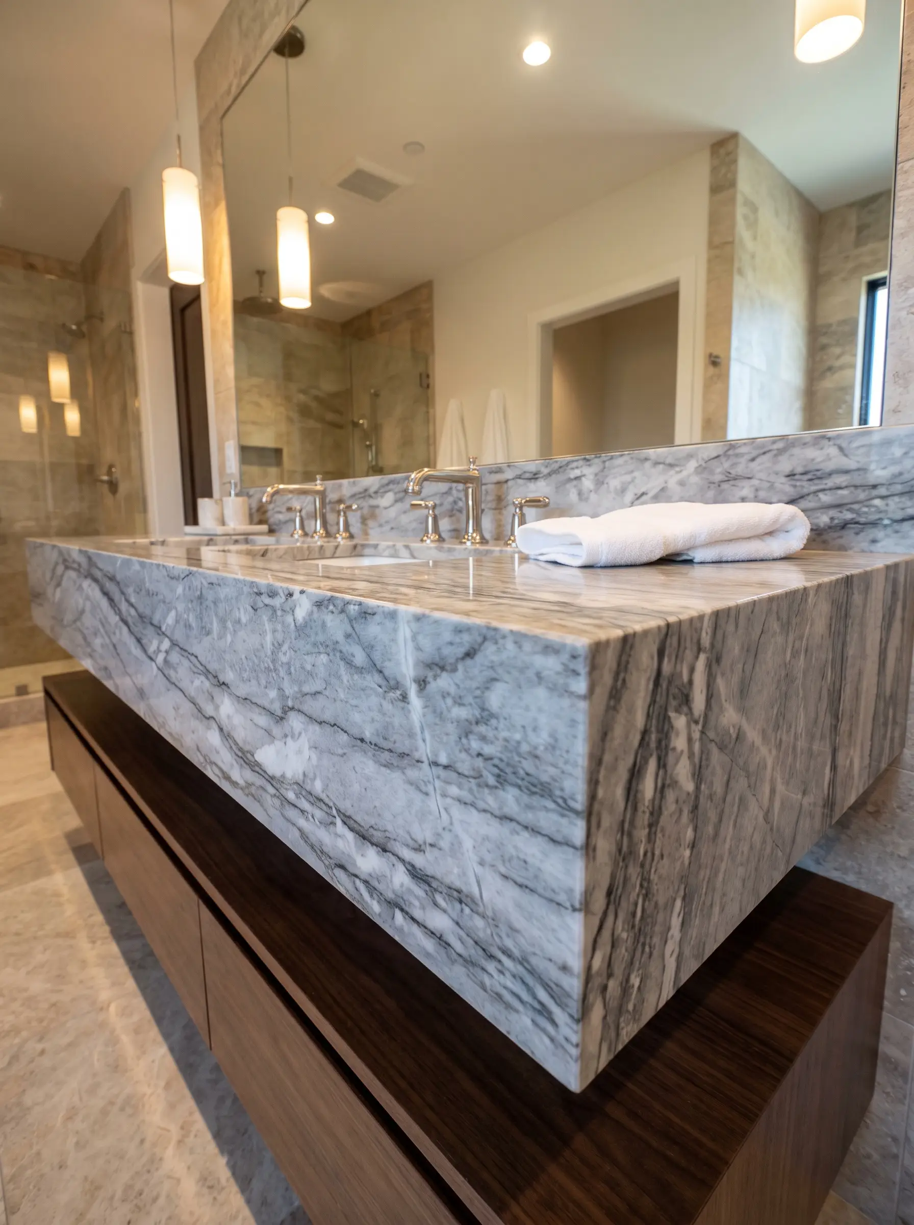 Heavy grey veining waterfalls over a thick mitered drop-edge marble countertop resting on a wooden vanity base with polished nickel widespread faucets.