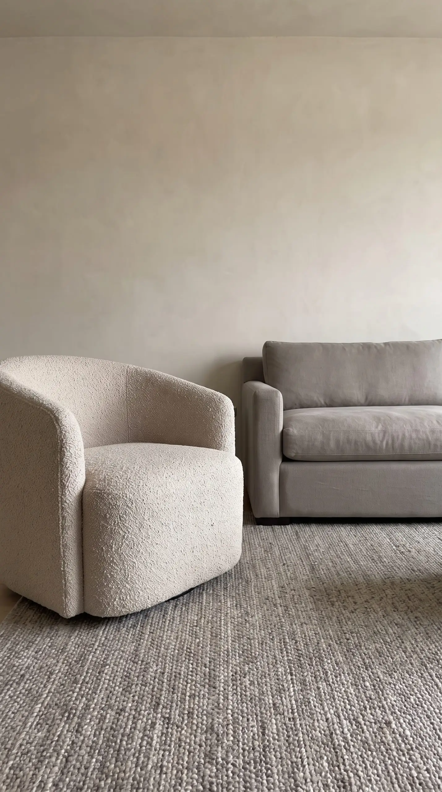 A nubby cotton boucle accent chair and a smooth heavyweight Belgian linen sofa sit on a coarse flat-weave wool rug against a smooth plaster wall.