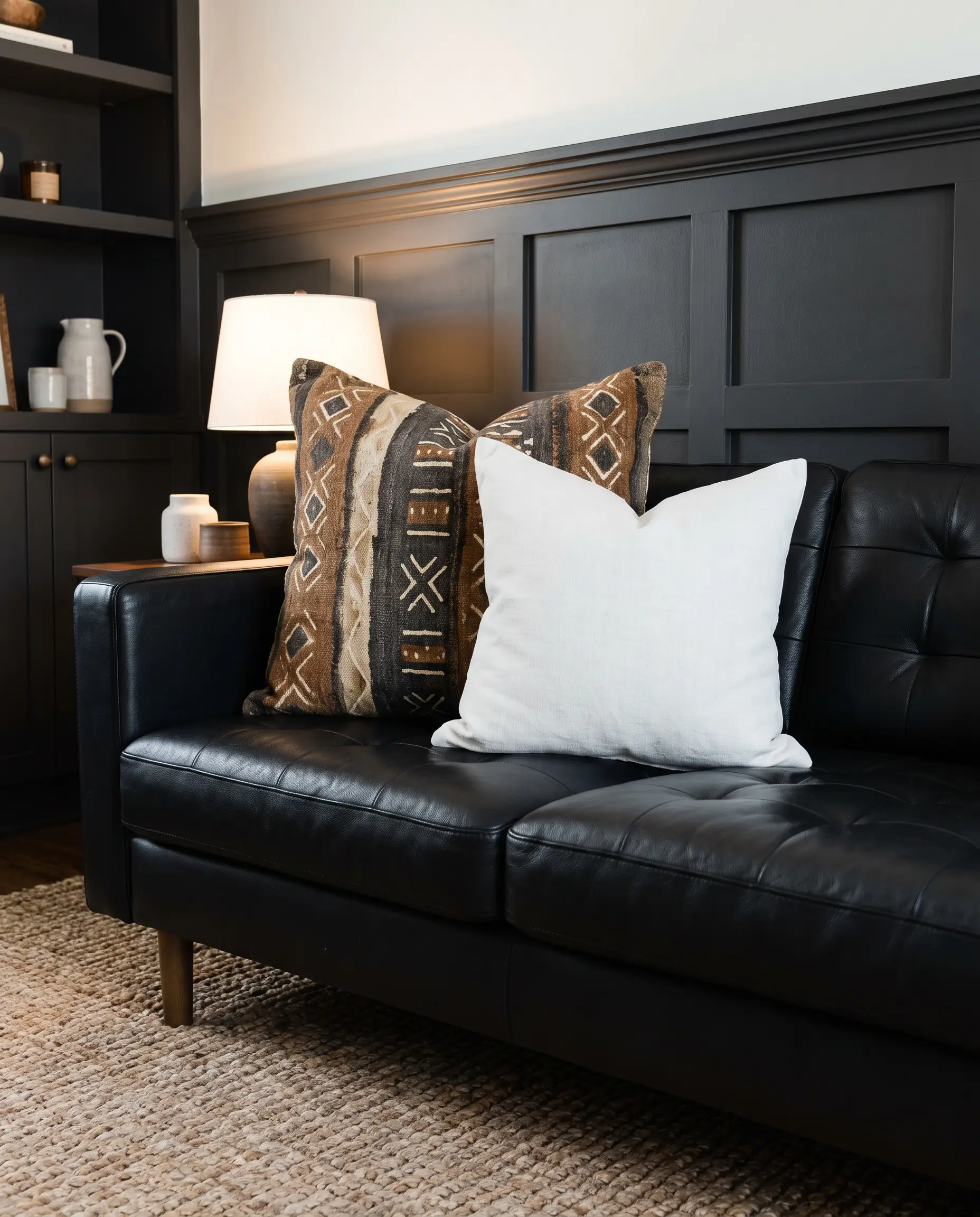 Geometric mudcloth throw pillows for leather couch arrangements layer with white linen on black upholstery above a soft jute rug and Tricorn Black accents.