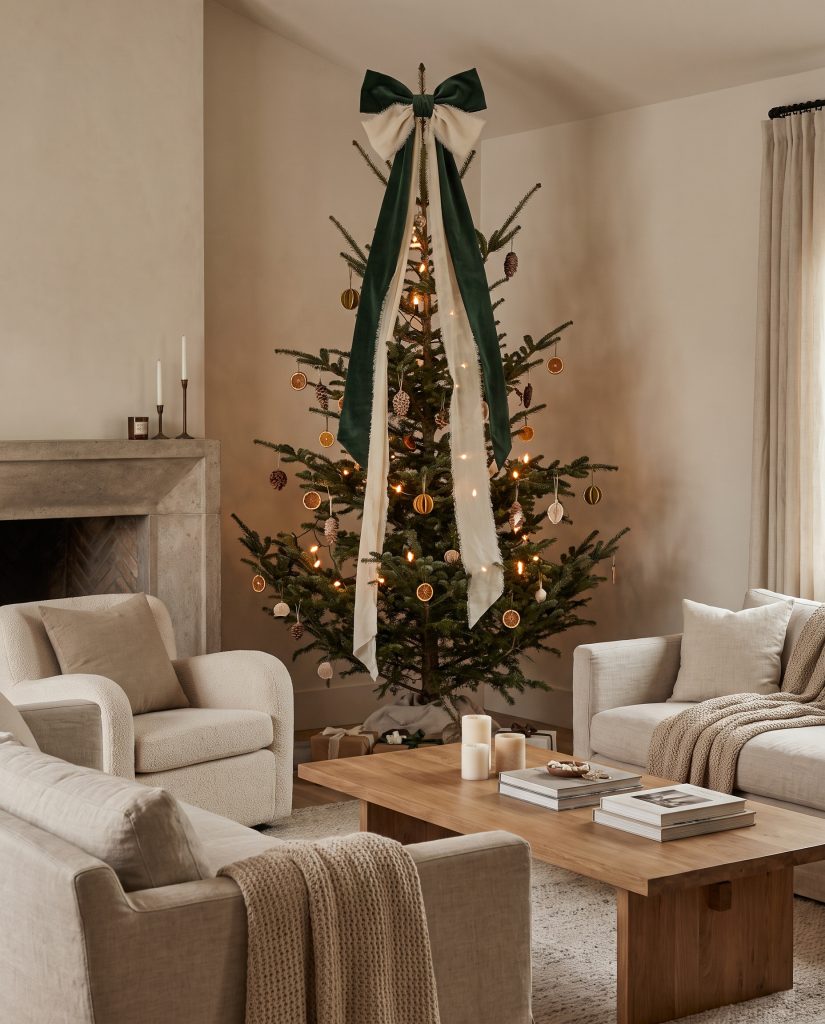 An oversized, relaxed bow crafted from heavy velvet and frayed silk chiffon crowns this 2026 Christmas tree decor, its long uneven tails trailing down sparse branches.