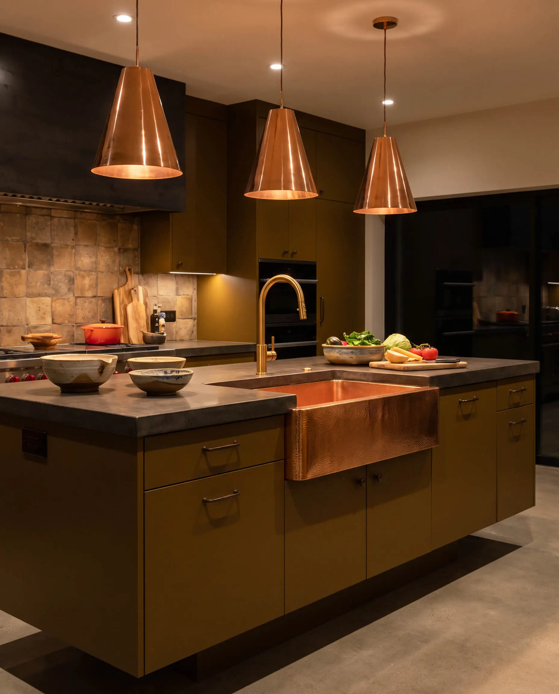 An exposed polished copper farmhouse sink and gleaming pendant lights contrast against muddy brown-mustard cabinetry in an elevated industrial prep zone.