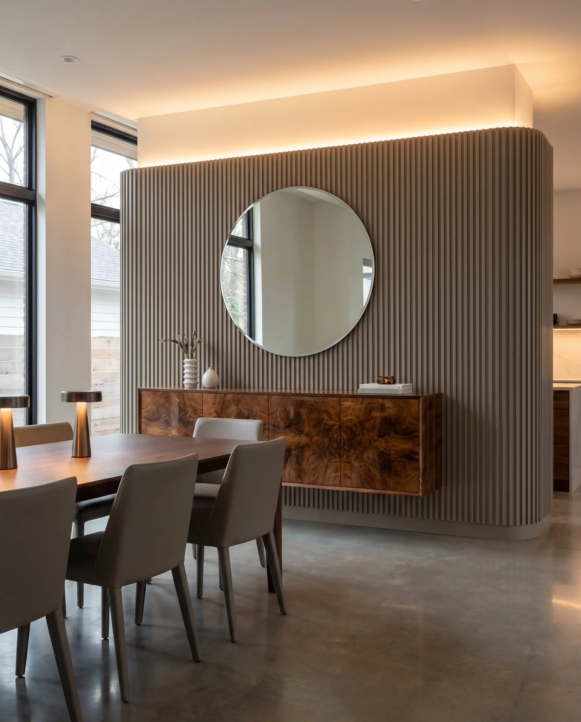 Raised fluted MDF core panels with a smooth paint-grade finish frame a highly polished burl wood credenza and sleek contemporary dining chairs.