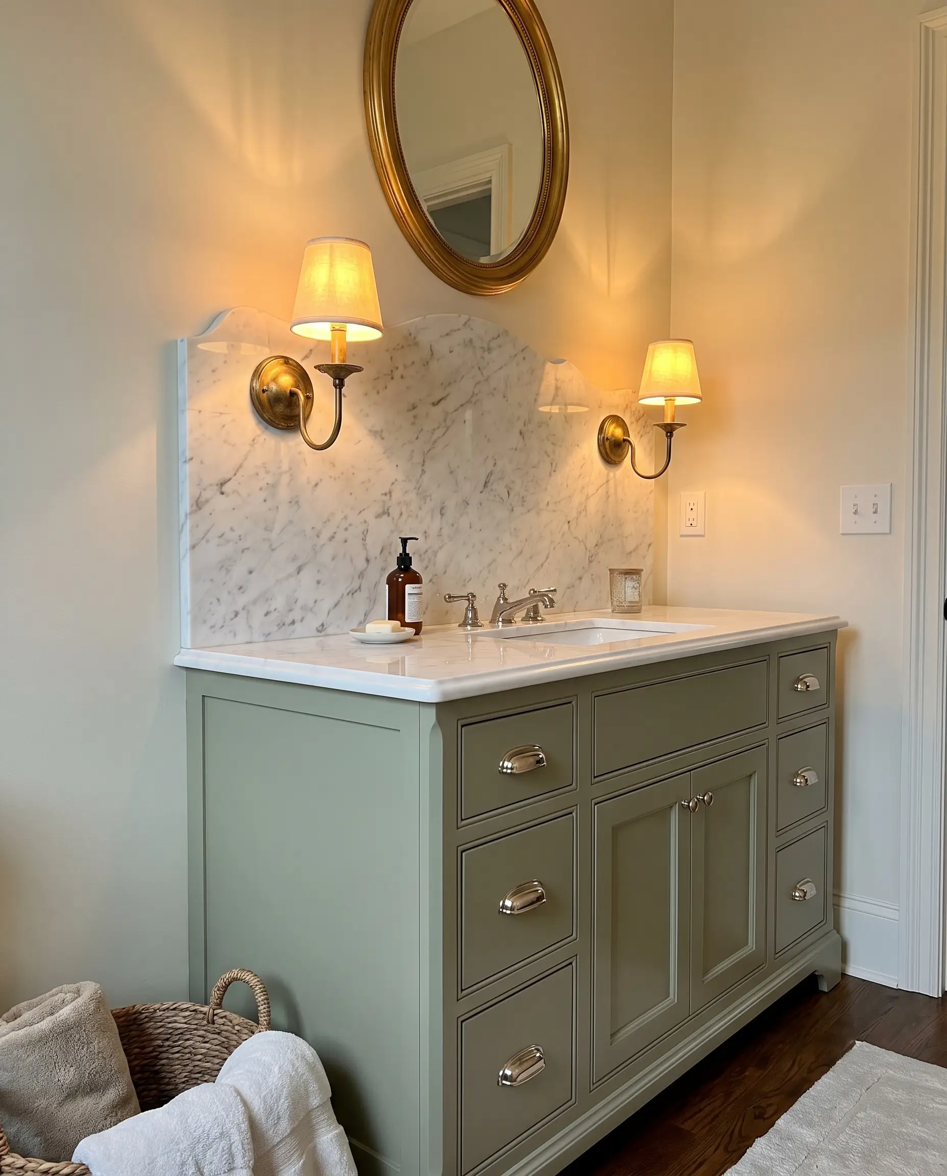Elegant brass sconces mount directly onto an 18-inch high Statuario marble backsplash featuring a custom scalloped edge above a muted green vanity base with polished nickel hardware.
