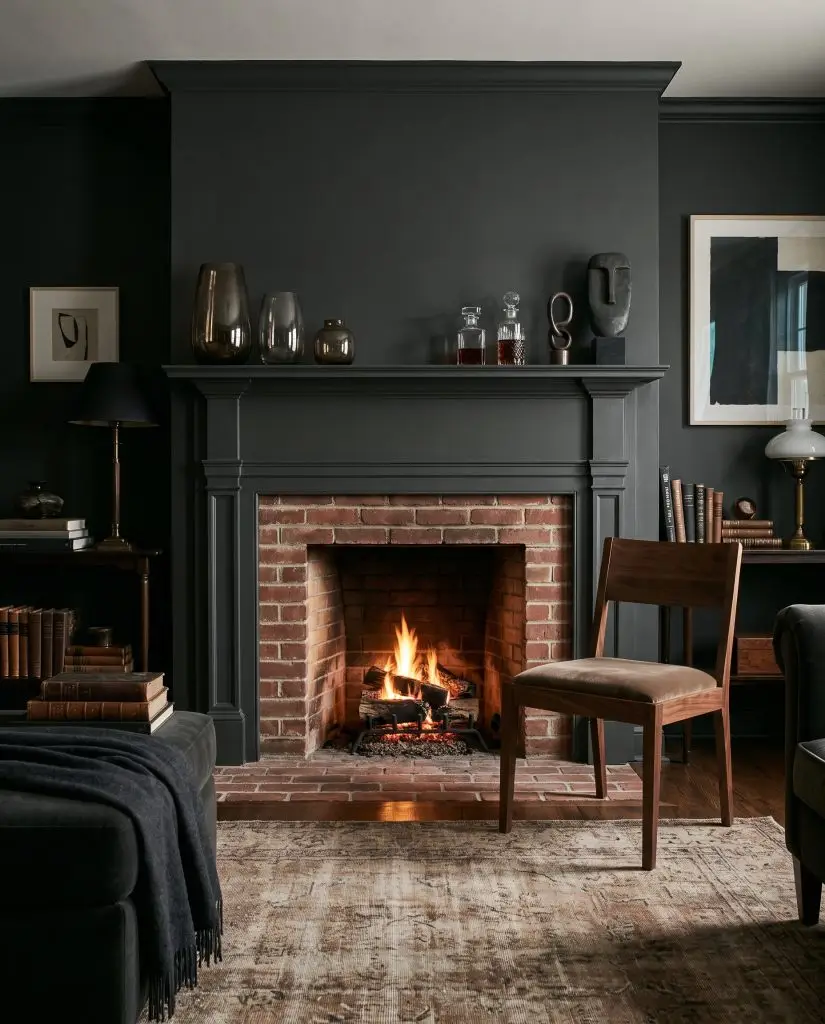 Smoked glass decor items rest on a Sherwin-Williams Greenblack painted mantel framing a natural red brick firebox, with a rich walnut side chair nearby.