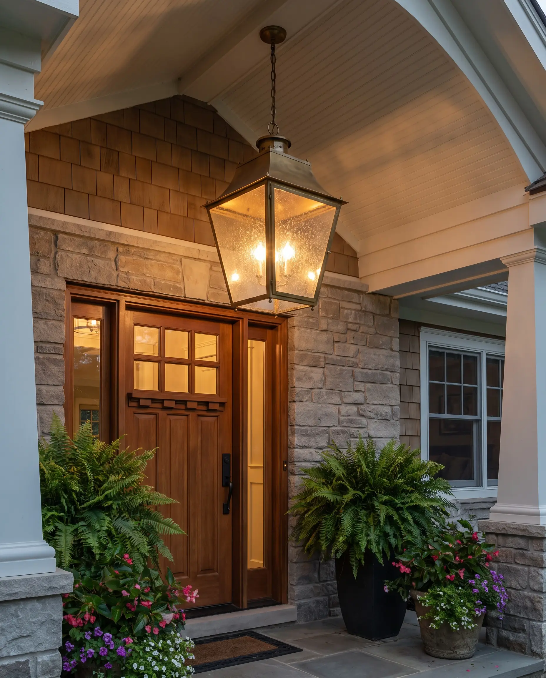 Front porch styling highlighting a substantial brass pendant lantern with seeded glass dropped from a covered ceiling, replacing standard flush-mount lighting.