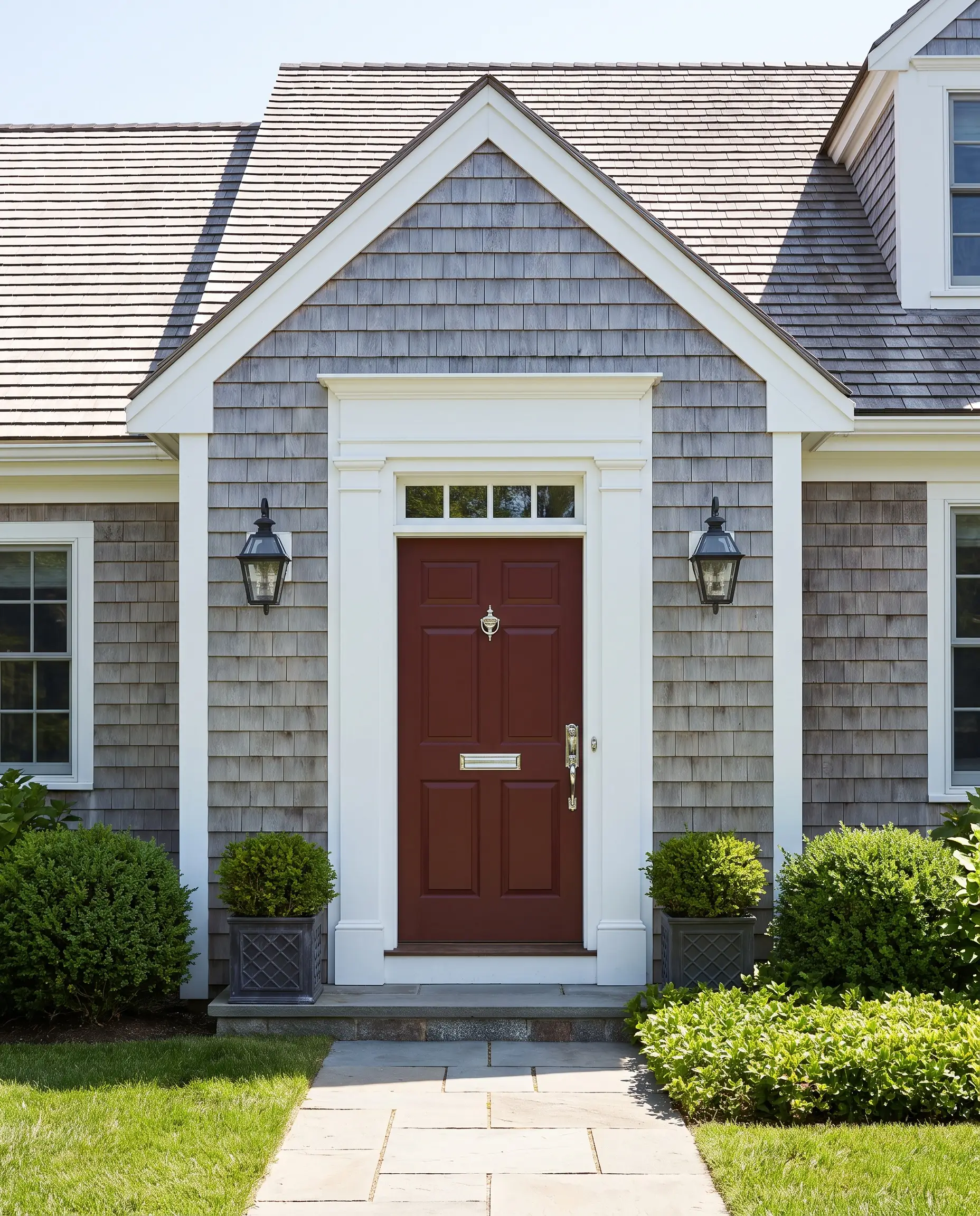 Crisp bright white trim and weathered gray shingles surround a Sun Dried Tomato red door outfitted with polished chrome hardware.