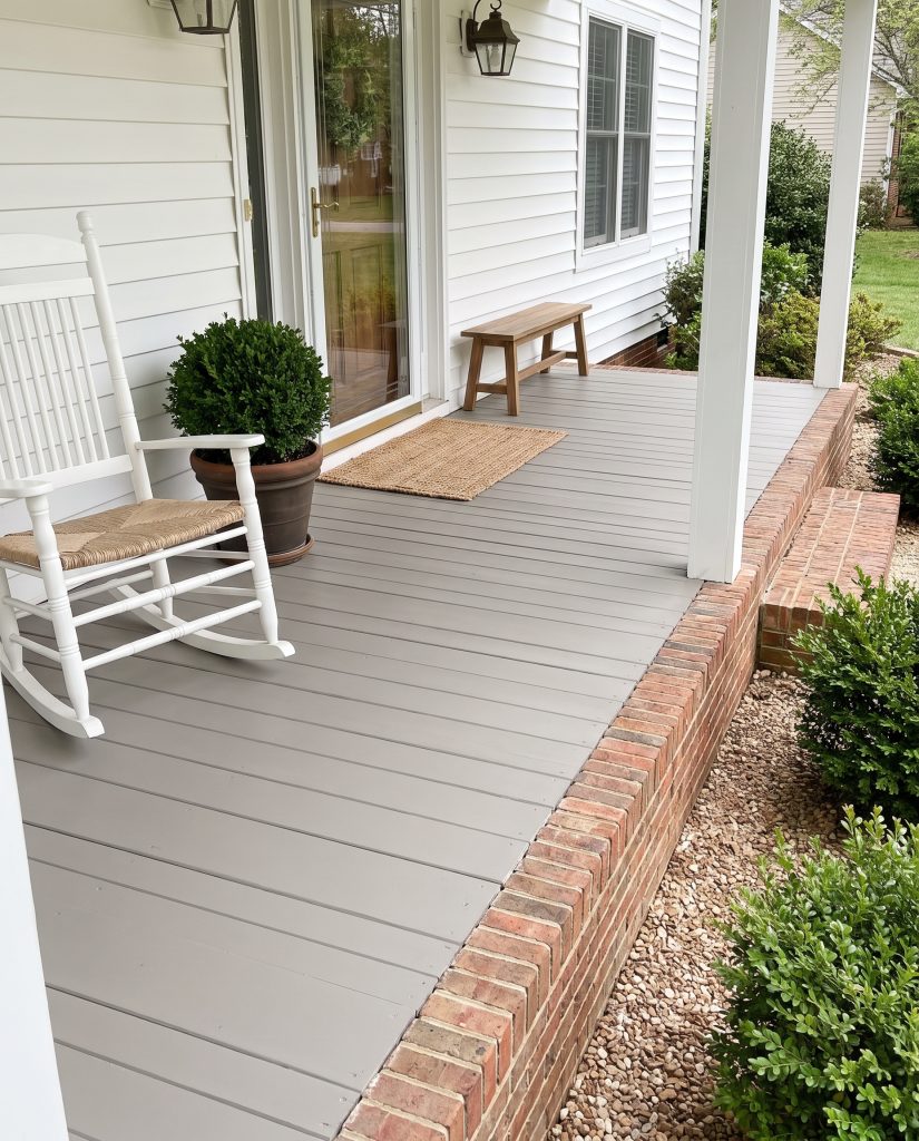 A dirt hiding porch paint in a smooth gray satin finish grounds a classic entryway featuring soft white siding and a wooden rocking chair.