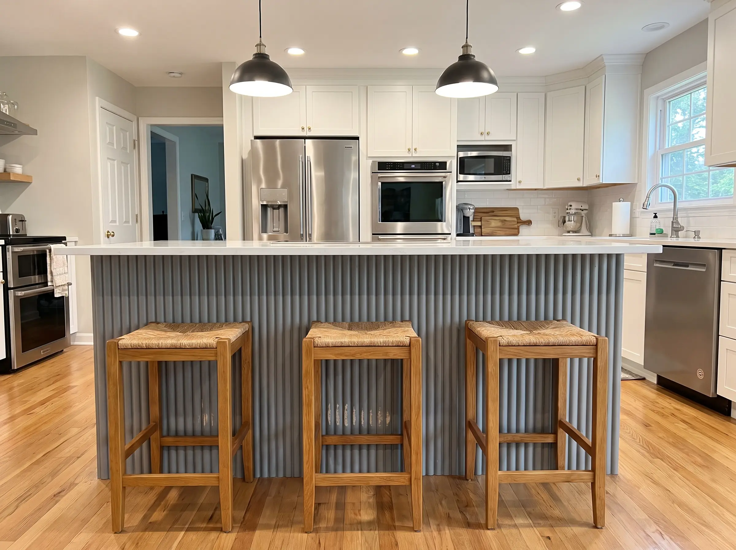 Heavy-duty PVC fluted panels wrap the back of a large kitchen island paired with warm oak barstools and crisp white quartz countertops.