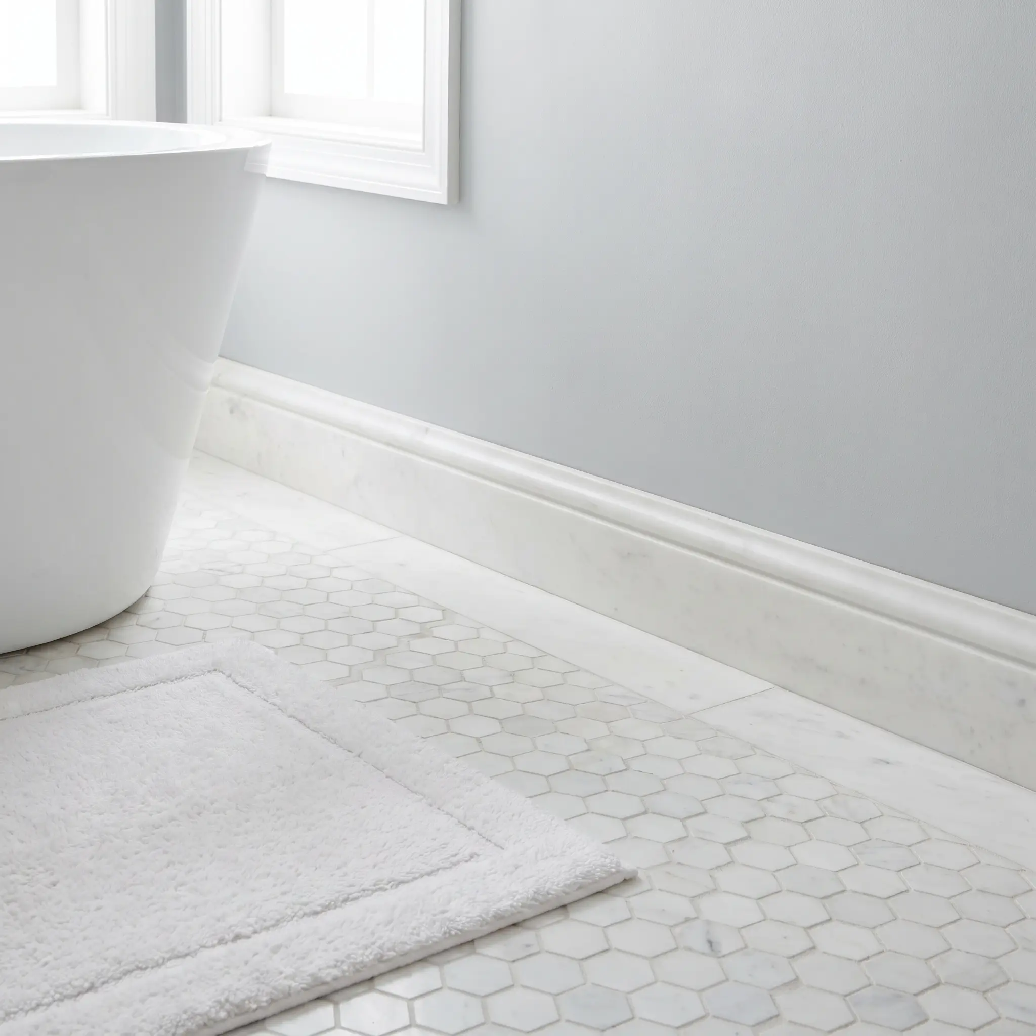 Delicate white marble hexagon floor mosaics are bordered by a solid six-inch high marble baseboard with a clean eased-edge profile against a smooth painted wall.