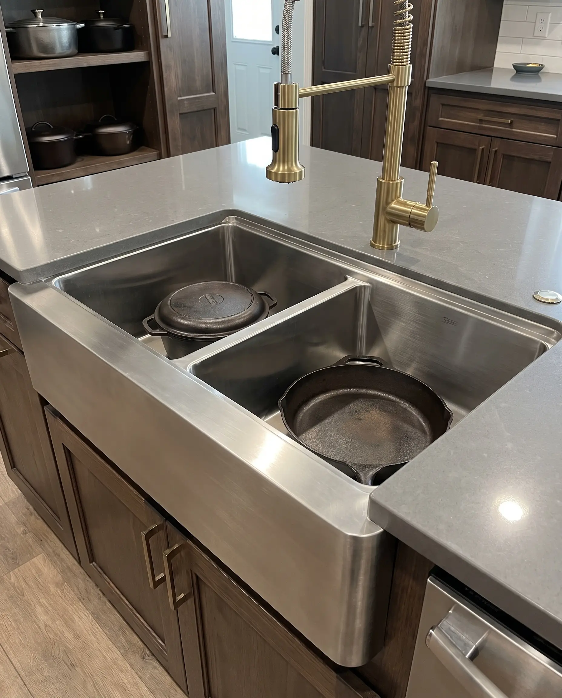 A heavy-duty 16-gauge stainless steel kitchen sink securely holds heavy cast iron cookware beneath a solid-brass PVD-coated faucet and quartz countertops.