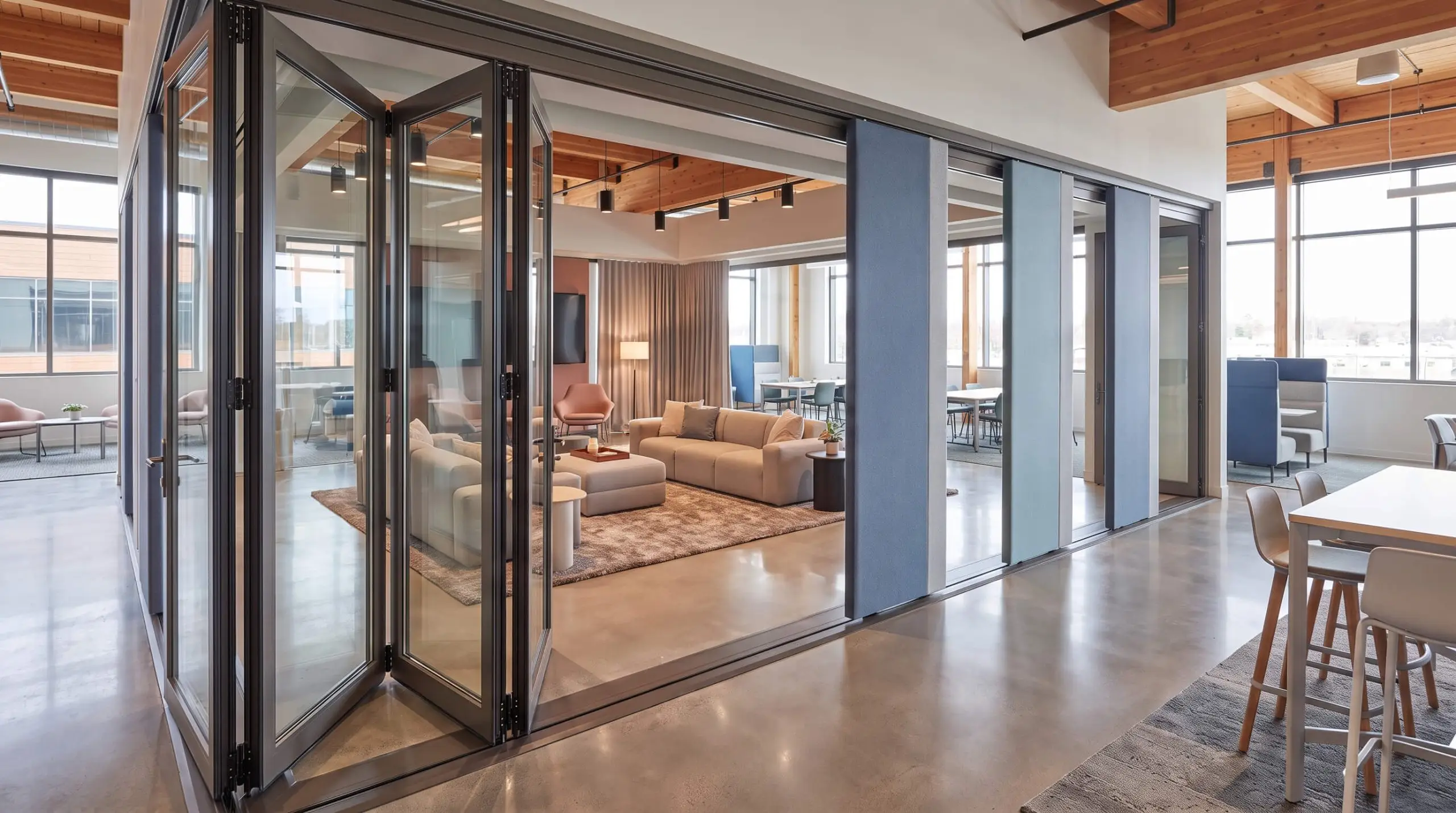 Double-glazed folding glass walls and fabric-wrapped movable acoustic panels divide a corporate town hall, exemplifying modular office design trends 2027.