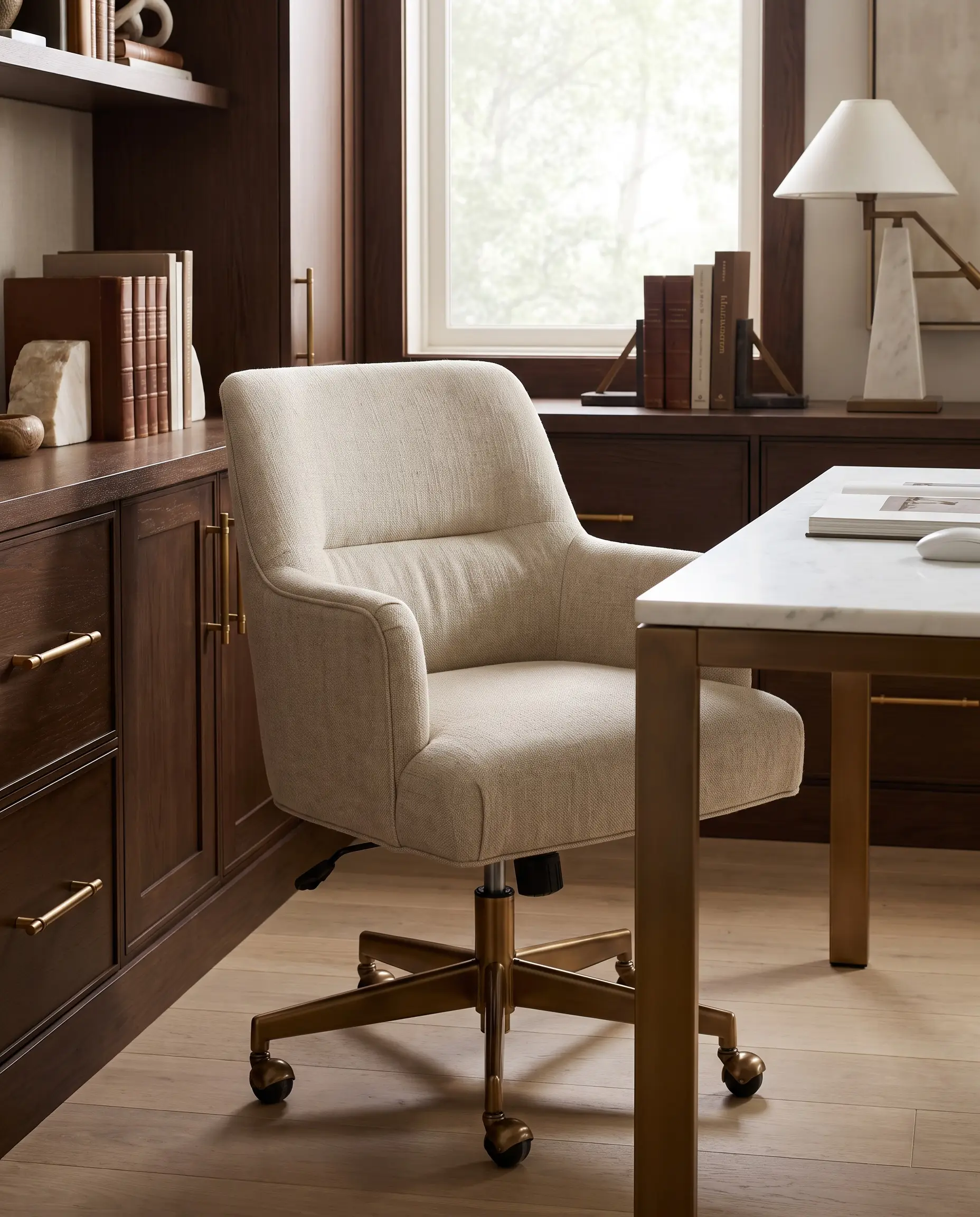 Fauteuil de bureau ergonomique habillé d'un épais lin belge avec piètement en bronze poli devant un bureau à plateau en marbre et menuiseries sur mesure.