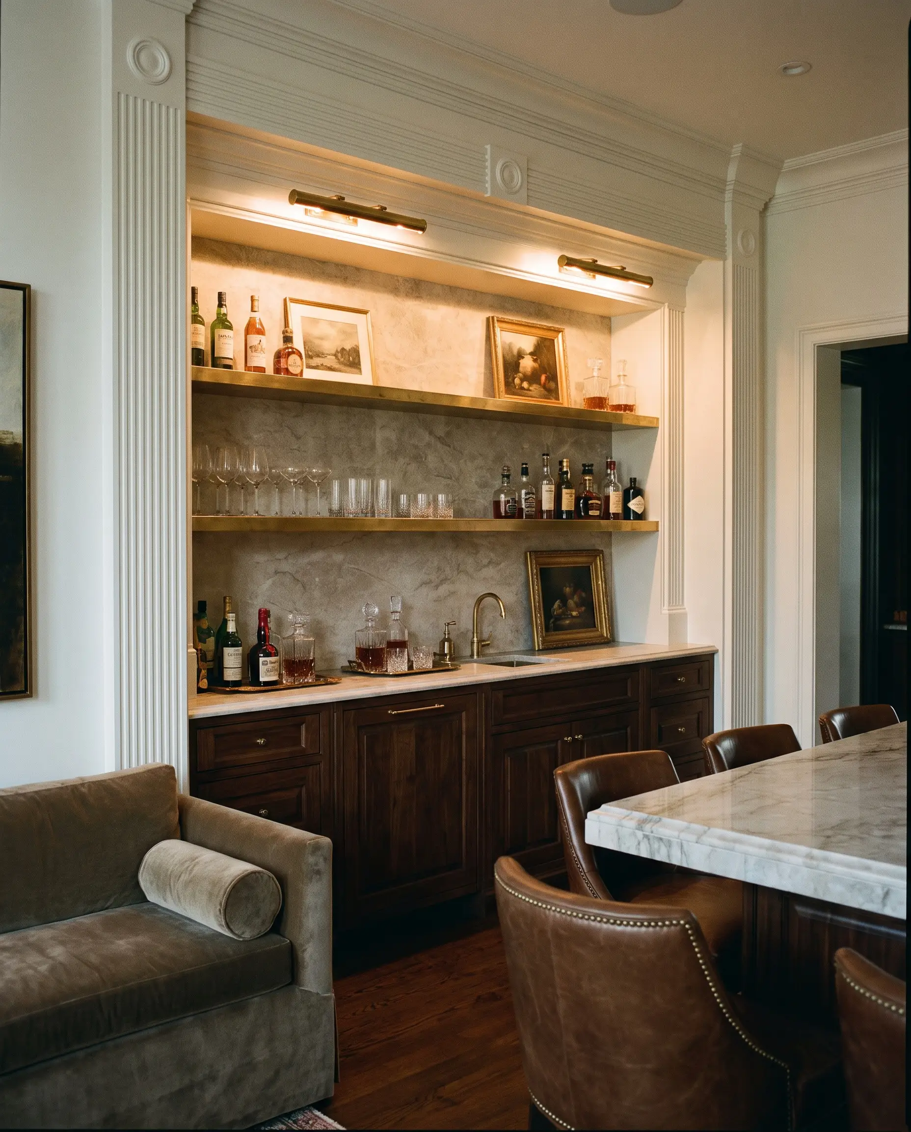 Traditional brass picture lights cast a warm low-glare glow over unlacquered brass floating shelves and elegant glassware in a rich upper bar alcove.