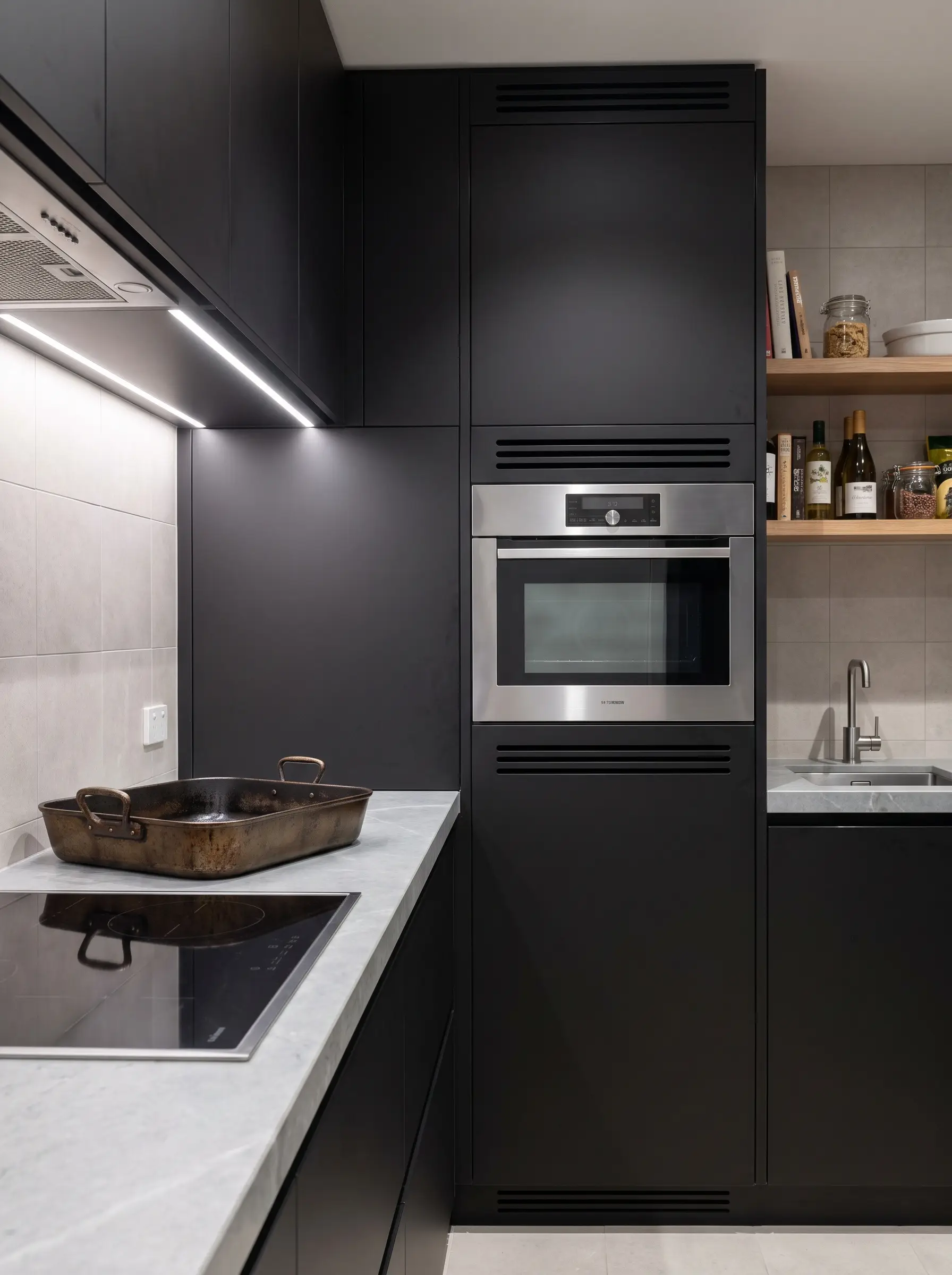 A sleek built-in secondary steam oven sits at exact eye-level within a stack of minimalist custom cabinetry beside a heavy cast iron roasting pan on a stone counter.