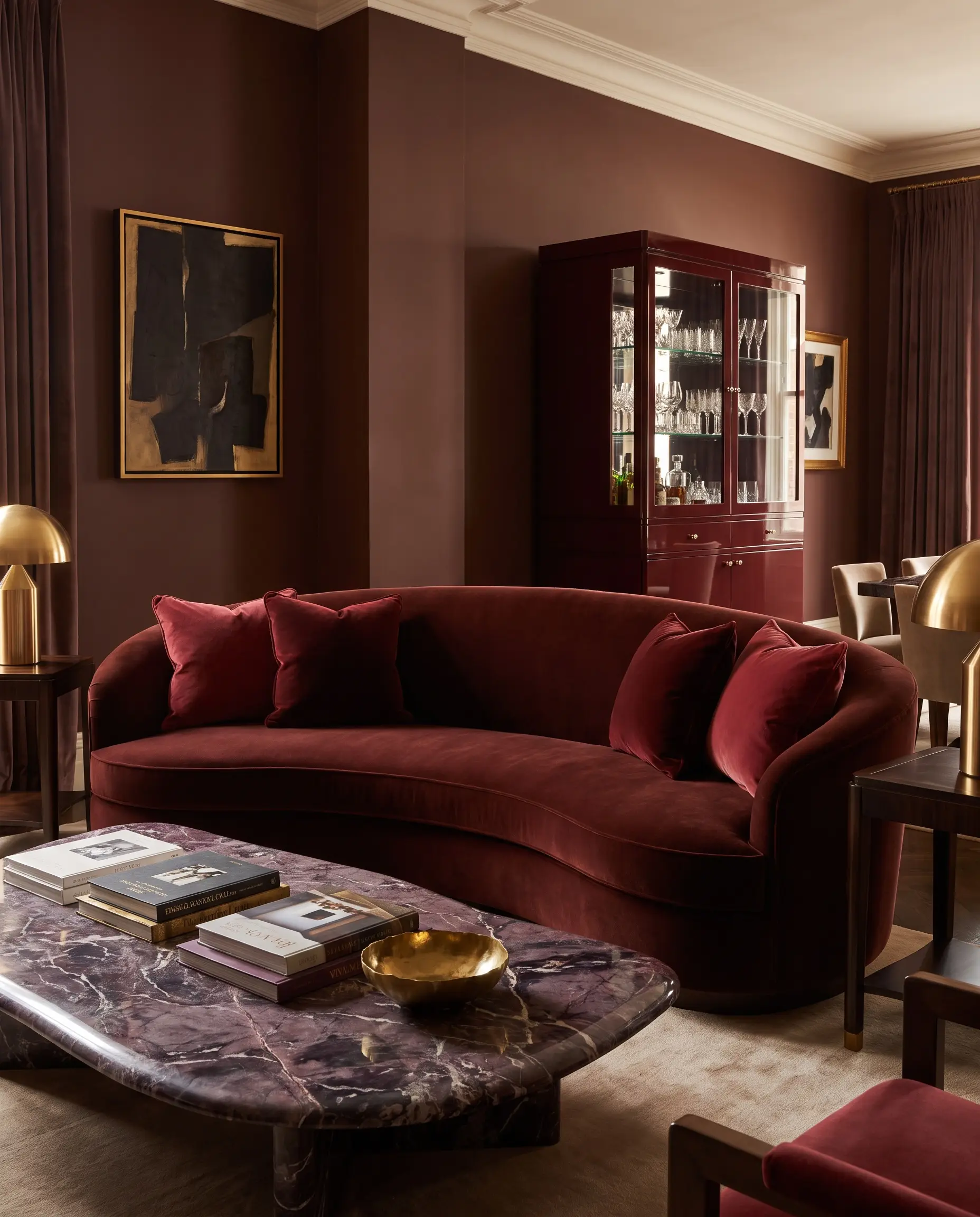 Forecasting 2027 home decor trends, this luxurious living room pairs Carnelian painted walls with an oxblood velvet curved sofa and a deeply veined aubergine marble coffee table.