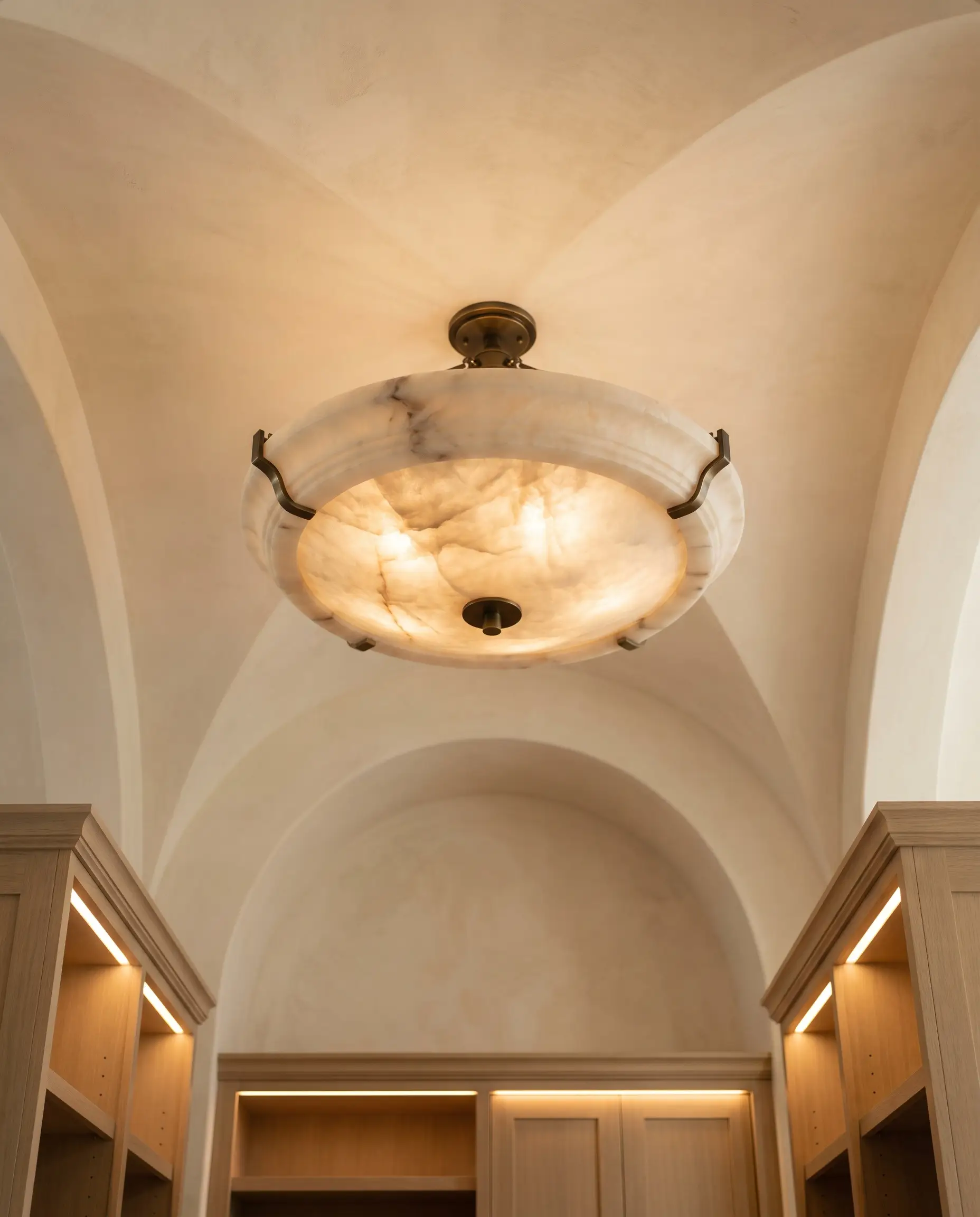 A massive carved Spanish alabaster flush-mount fixture with unlacquered brass standoffs casts an ambient glow over bespoke white oak mudroom cabinetry.
