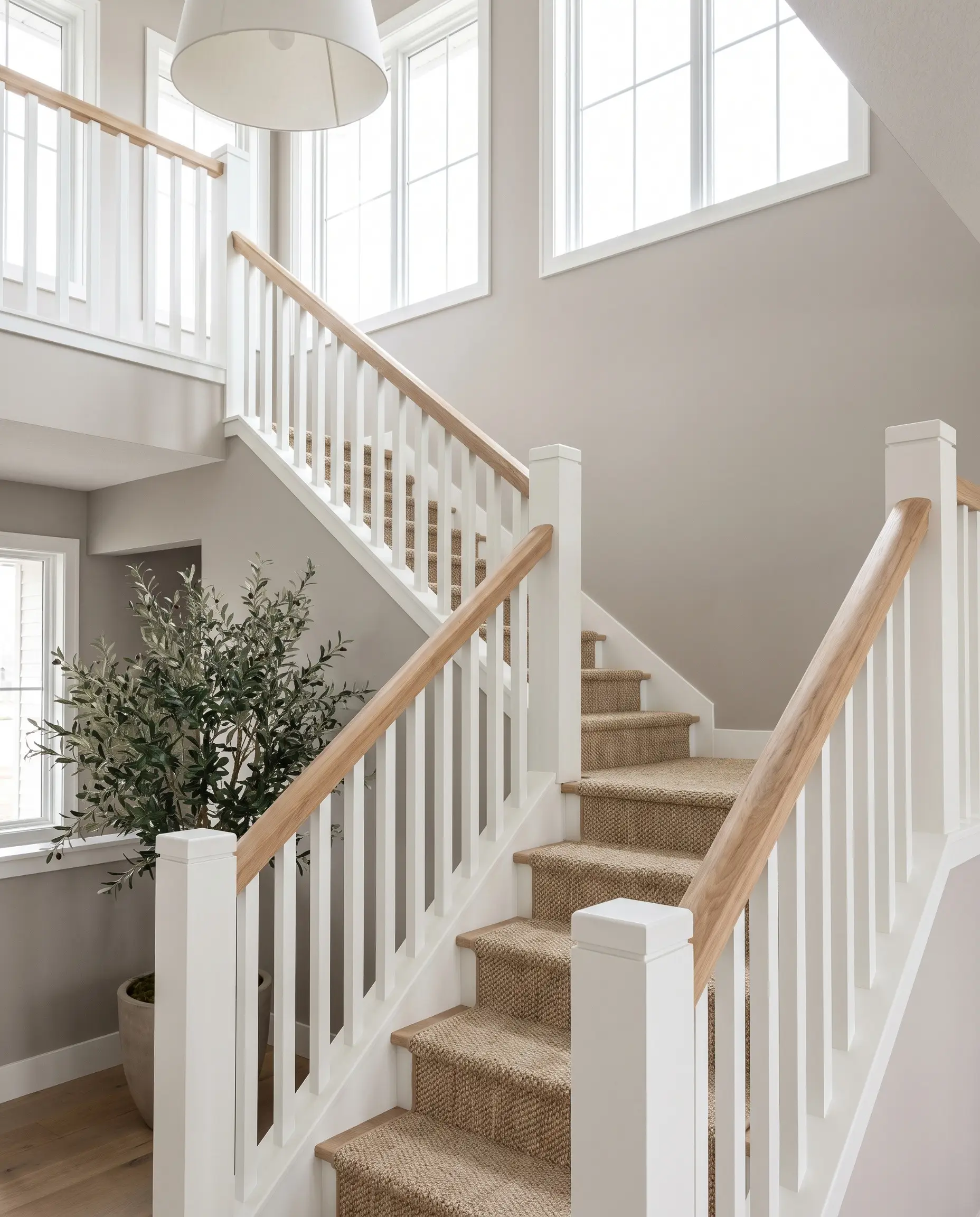 Crisp square poplar newel posts and balusters painted in Chantilly Lace support a continuous raw-oiled white oak handrail above a woven natural fiber stair runner.