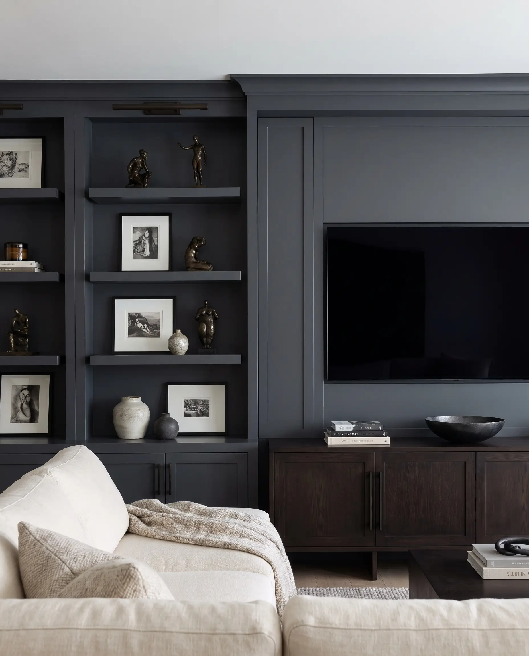 A camouflaged media wall painted in Benjamin Moore Cheating Heart conceals a flush-mounted screen above an espresso-stained credenza styled with blackened steel accents.