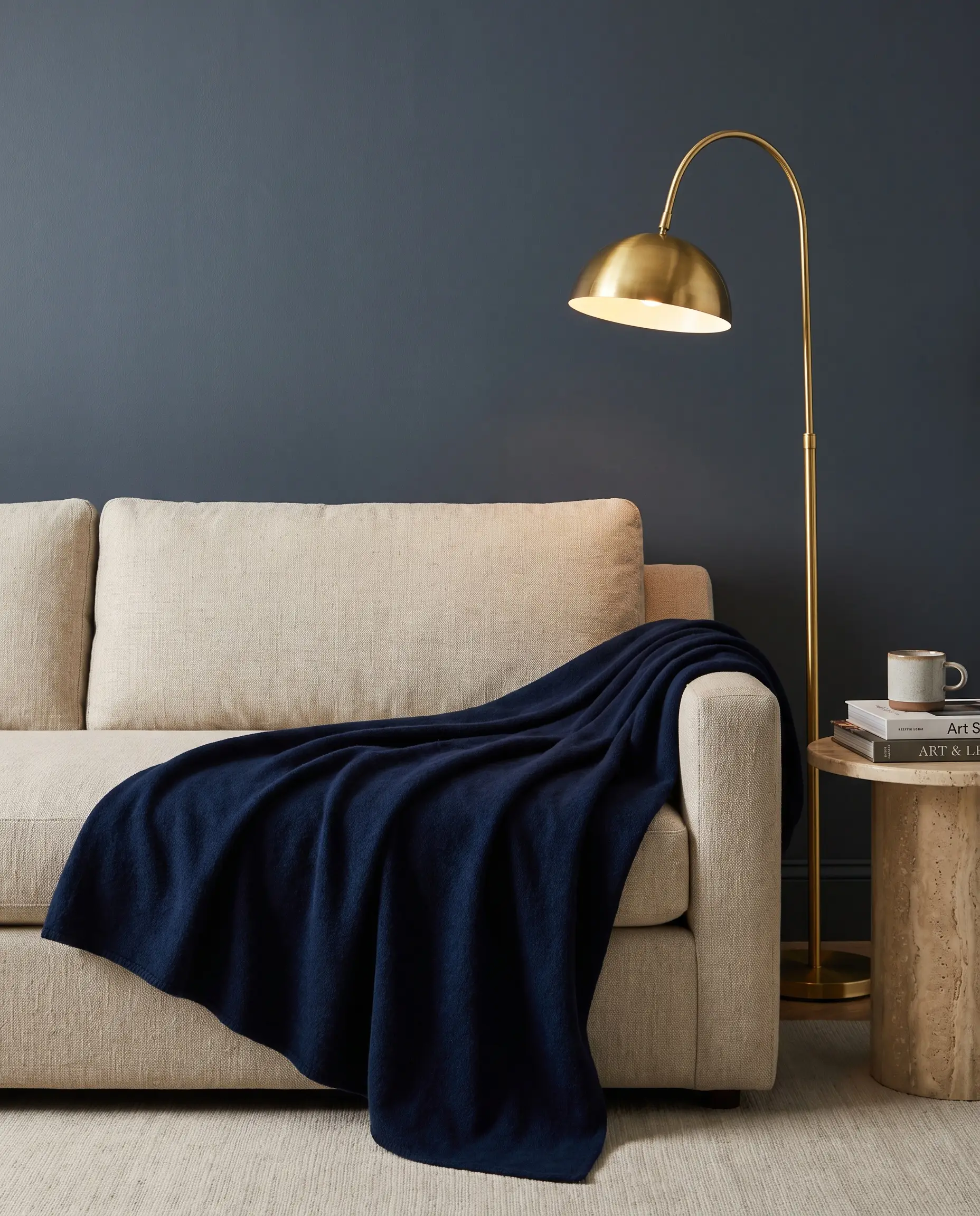 Plaid en laine bleu indigo profond drapé sur un canapé écru devant un mur peint en Hale Navy de Benjamin Moore avec lampe en laiton poli.
