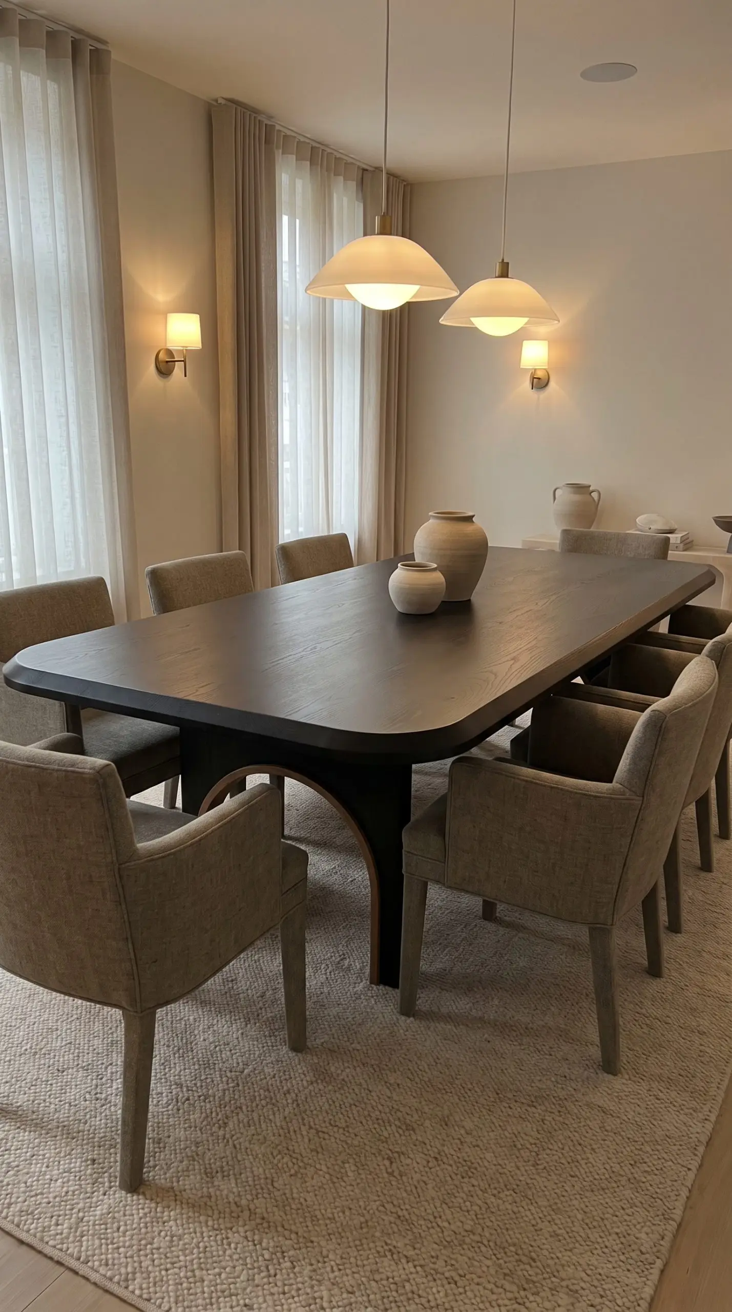 The latest dining room furniture features a bespoke ebonized oak table with deep-radius soft-square corners and architectural bentwood joinery over a textured rug.